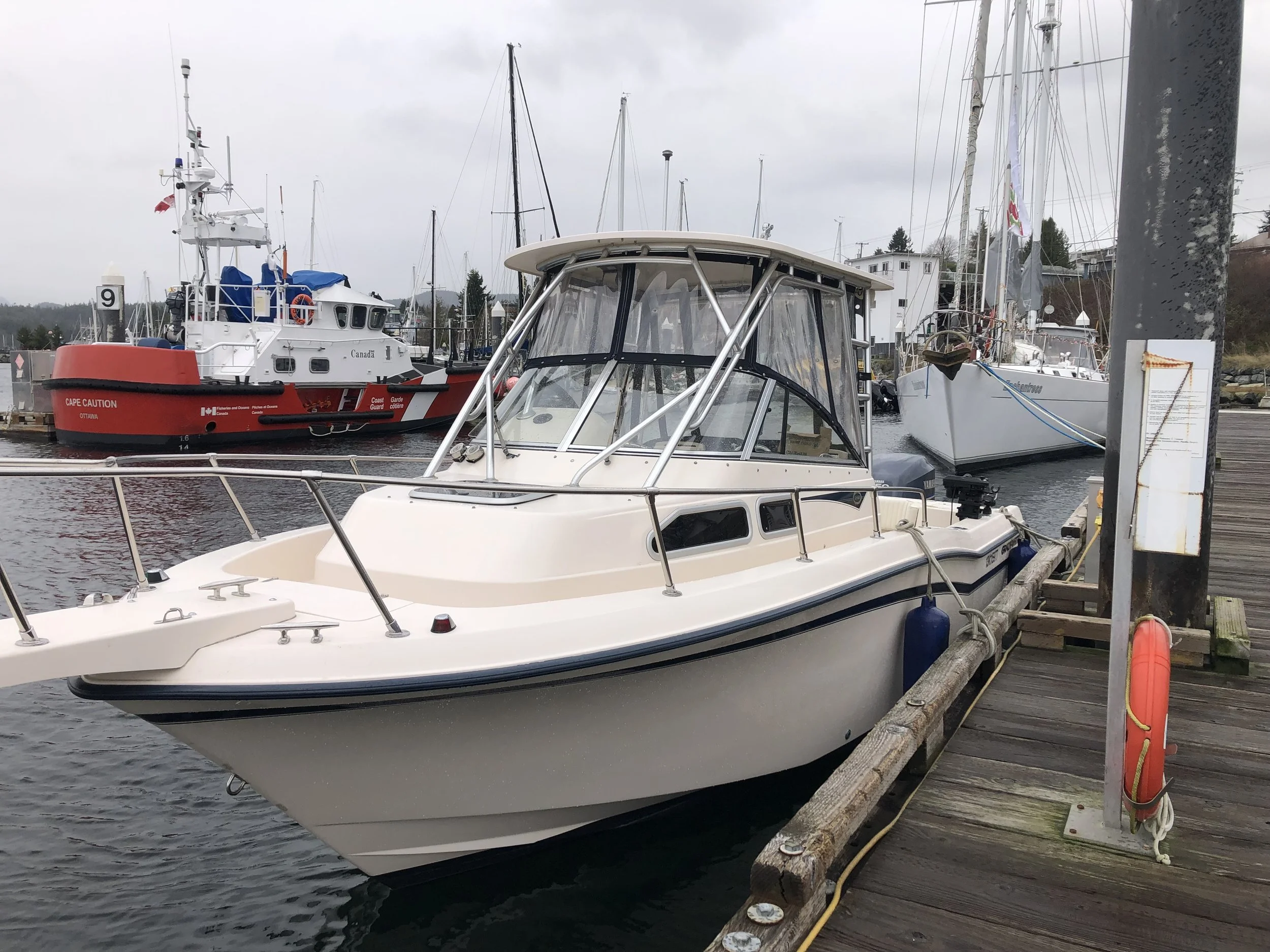 A Grady White fishing boat docked at a marina with other boats and sailboats in the background under cloudy skies.