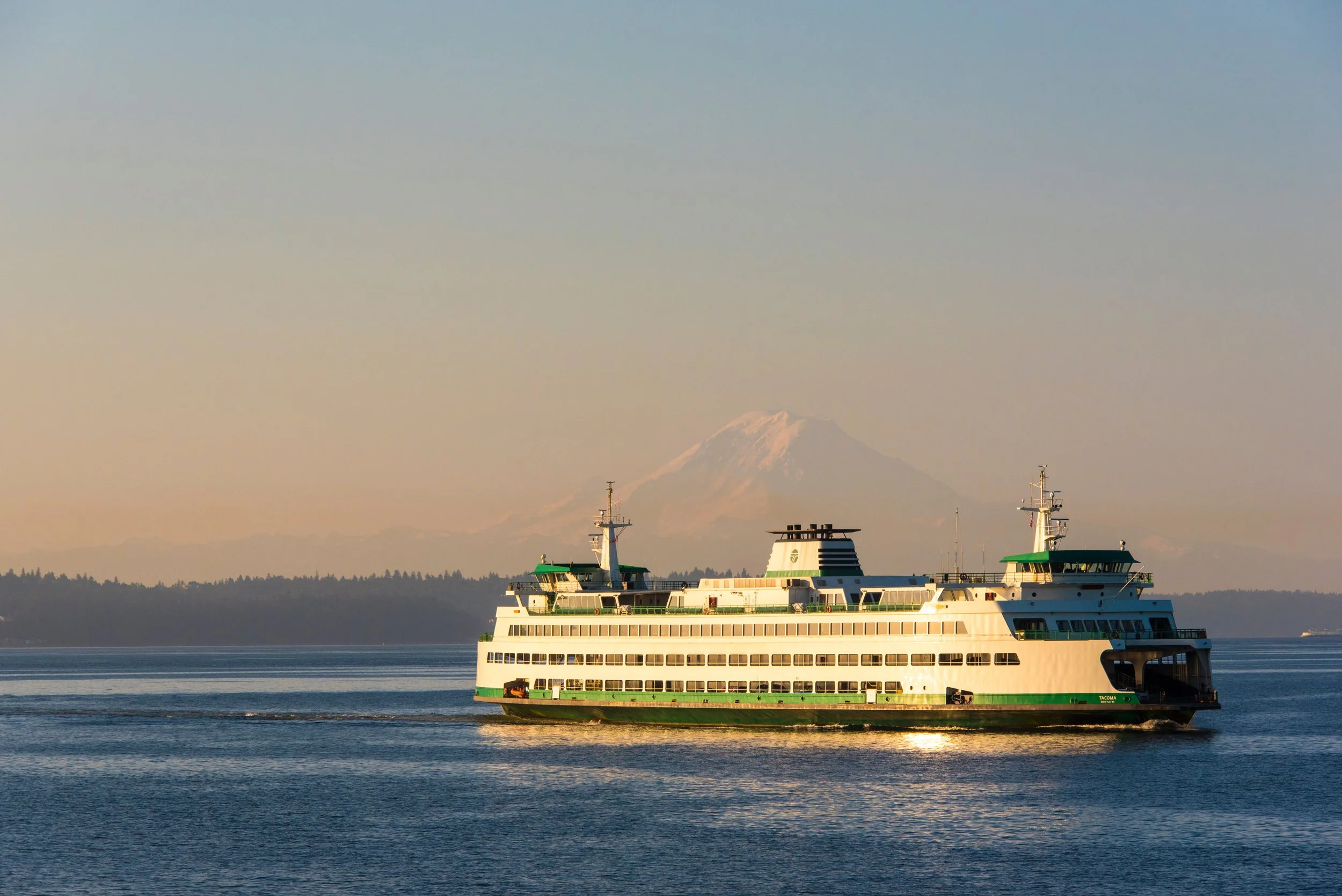Ferry boat sailing on water with Mount Rainier in background during sunset.