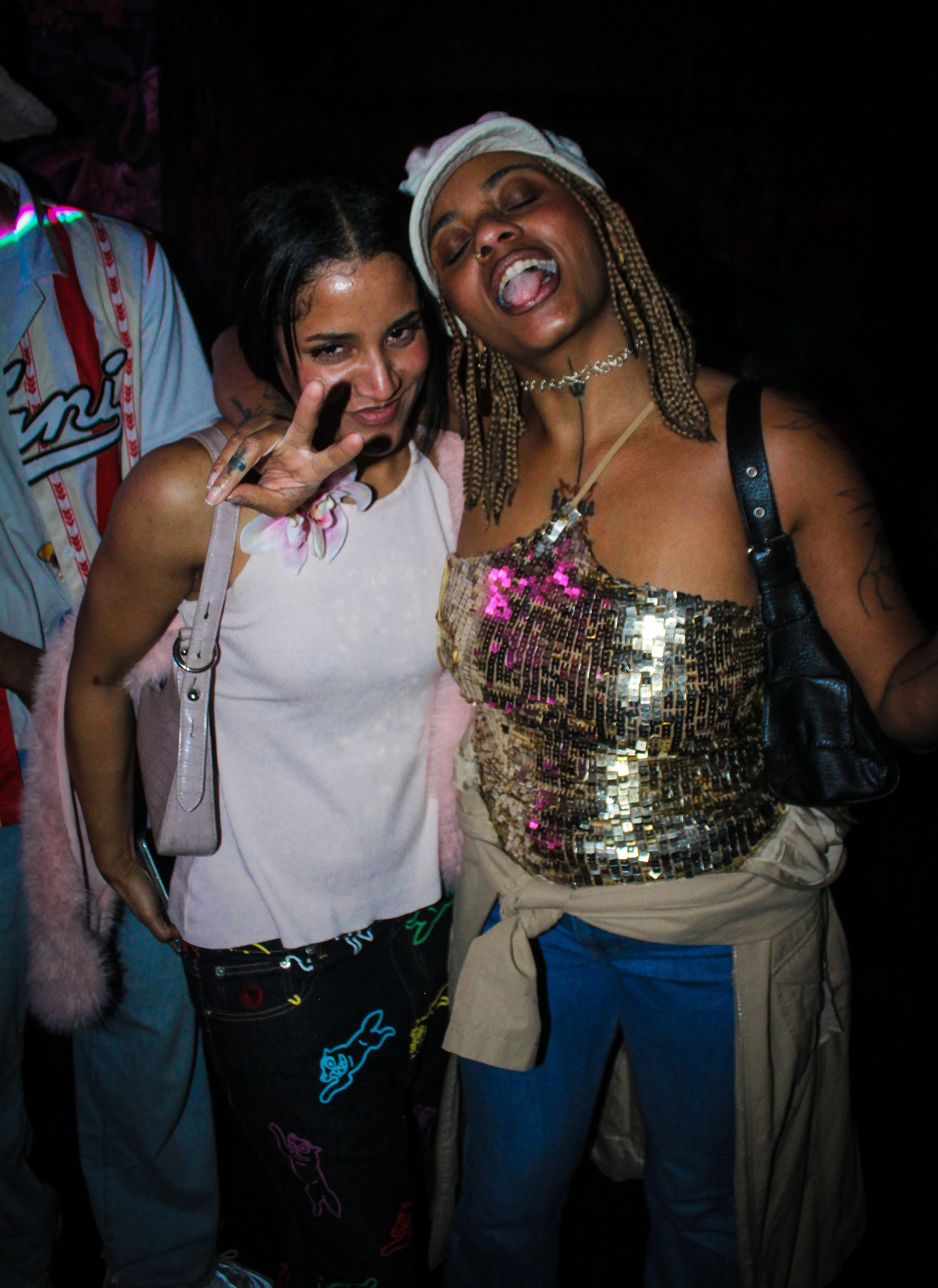 Two women at a party, one making a peace sign, both smiling and enjoying themselves.
