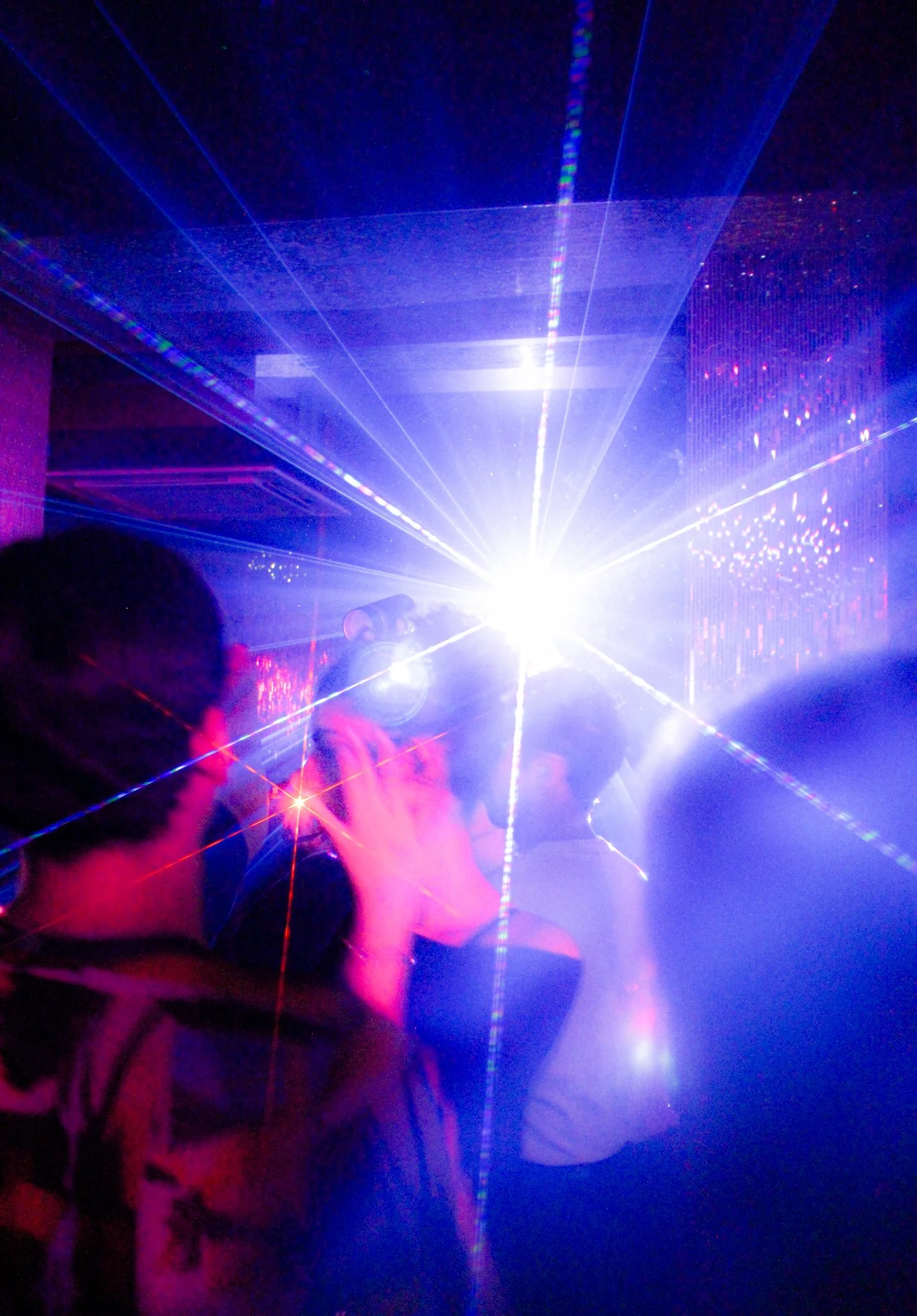 People dancing at a nightclub with bright laser lights and colorful reflections.
