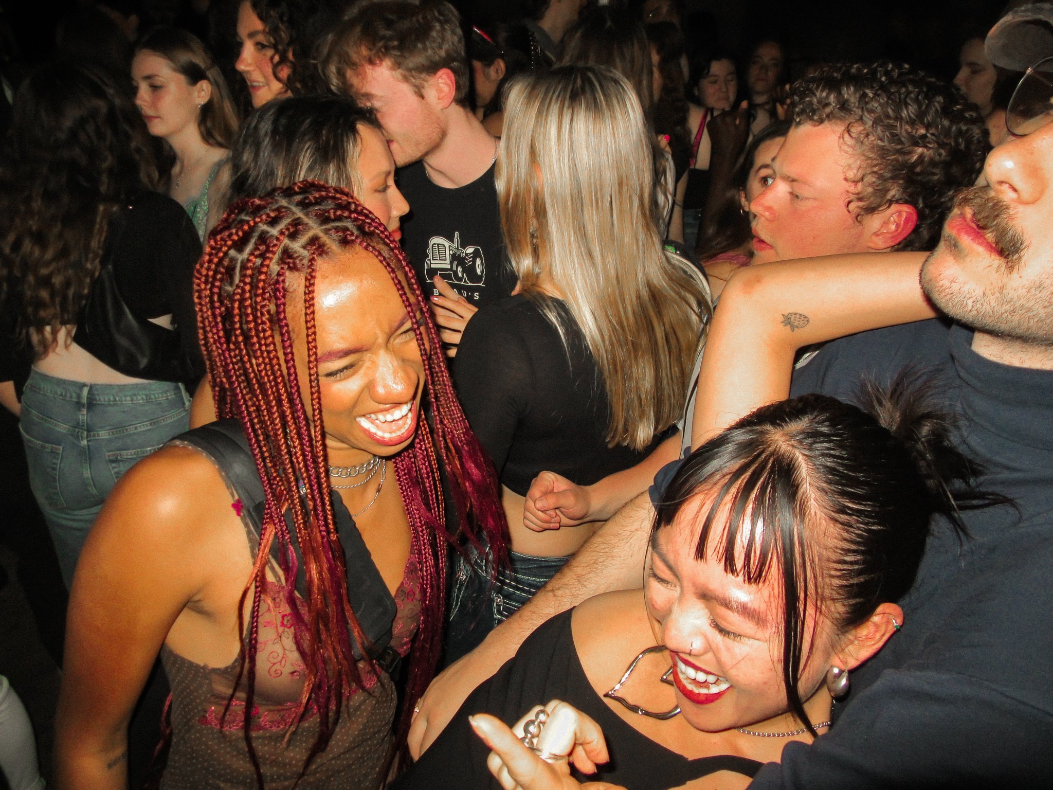 A group of people enjoying a lively moment at a party or concert, with smiling and laughing individuals in close proximity.