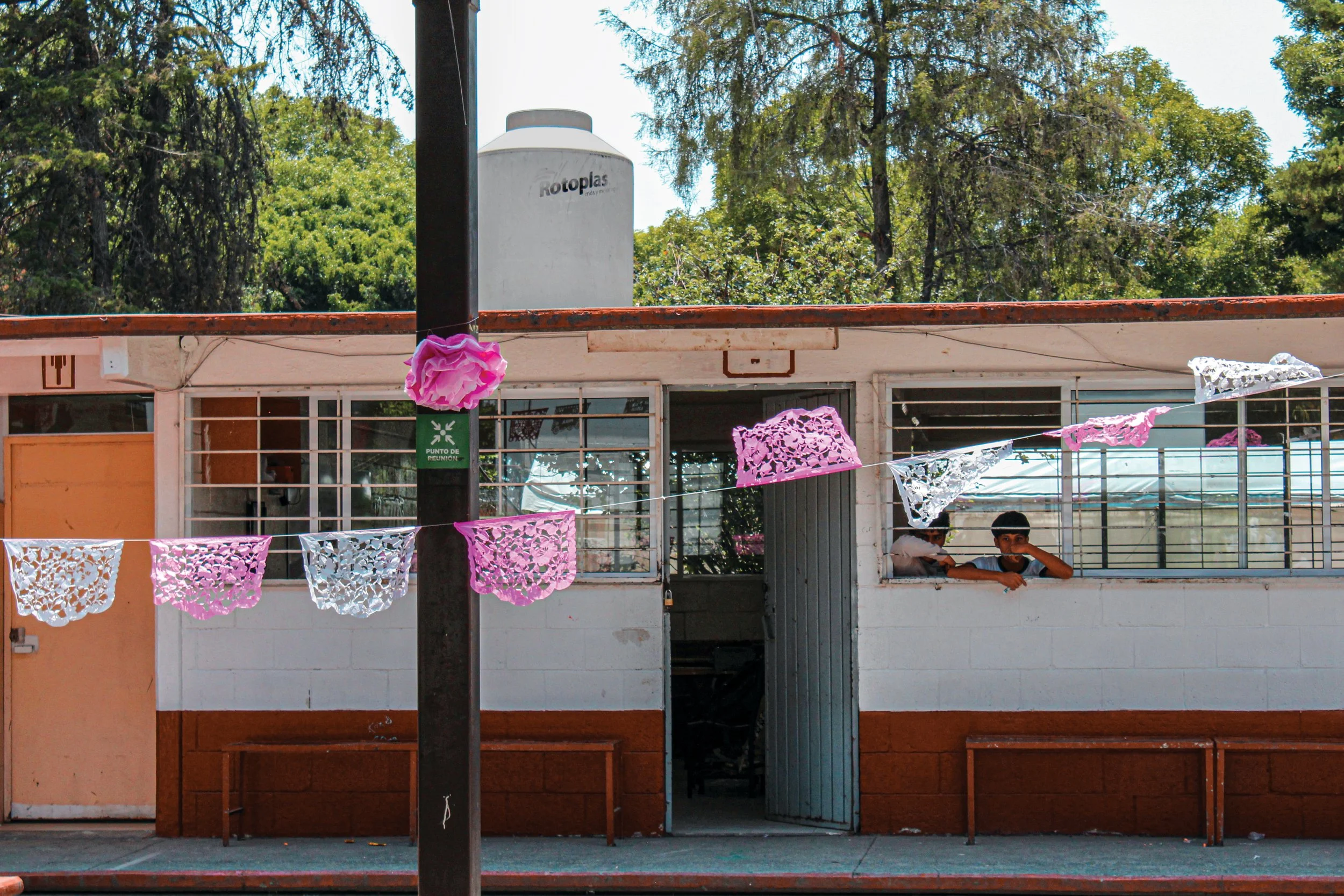 Children playing in a classroom with pink and white papel picado decorations hanging outside the window.