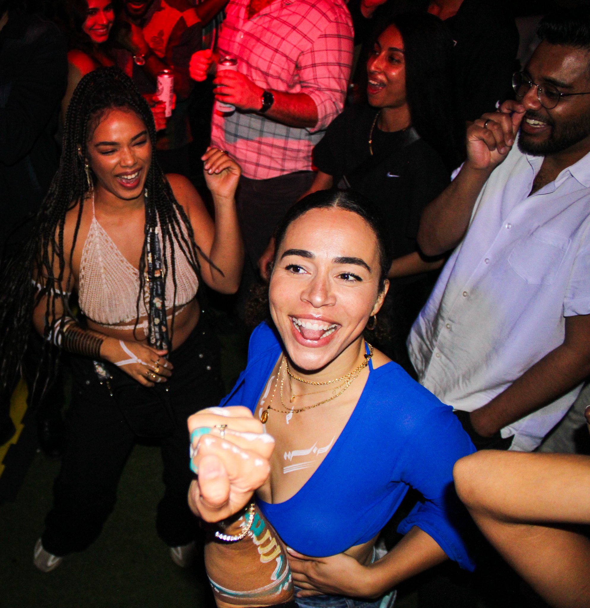 Group of people dancing and celebrating at a party, with a woman in a blue top smiling in the foreground.