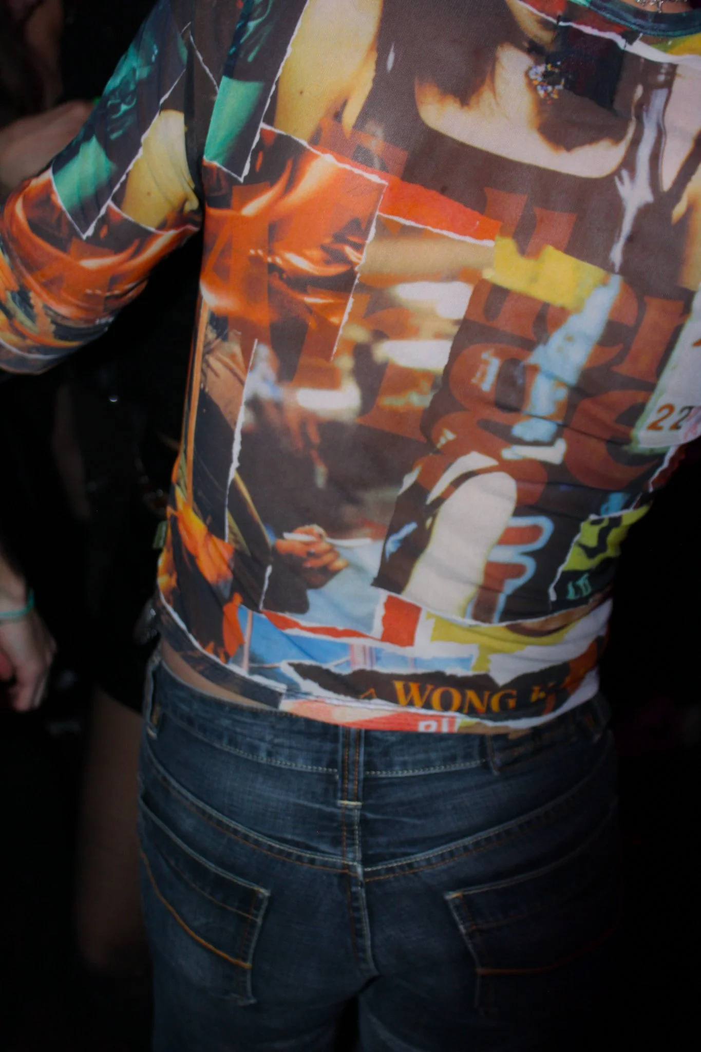 Person wearing a colorful shirt with abstract designs and dark jeans, seen from behind.
