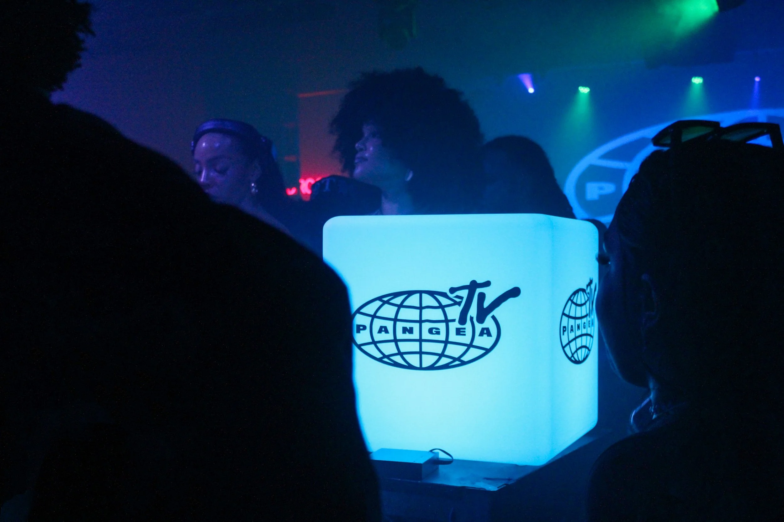 A DJ booth with a glowing screen displaying MTV Africa logo, with people in the background at a dimly lit nightclub or event.