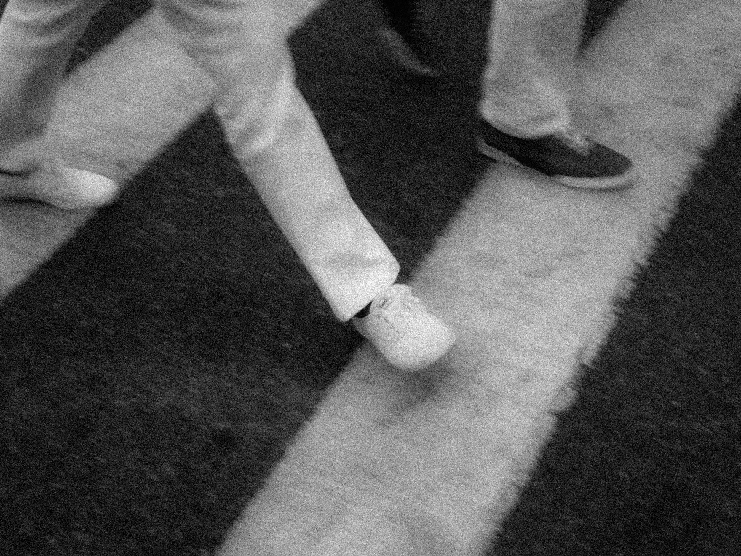 Close-up of a person's legs with one foot stepping on a black and white striped carpet, wearing light-colored pants and white sneakers.