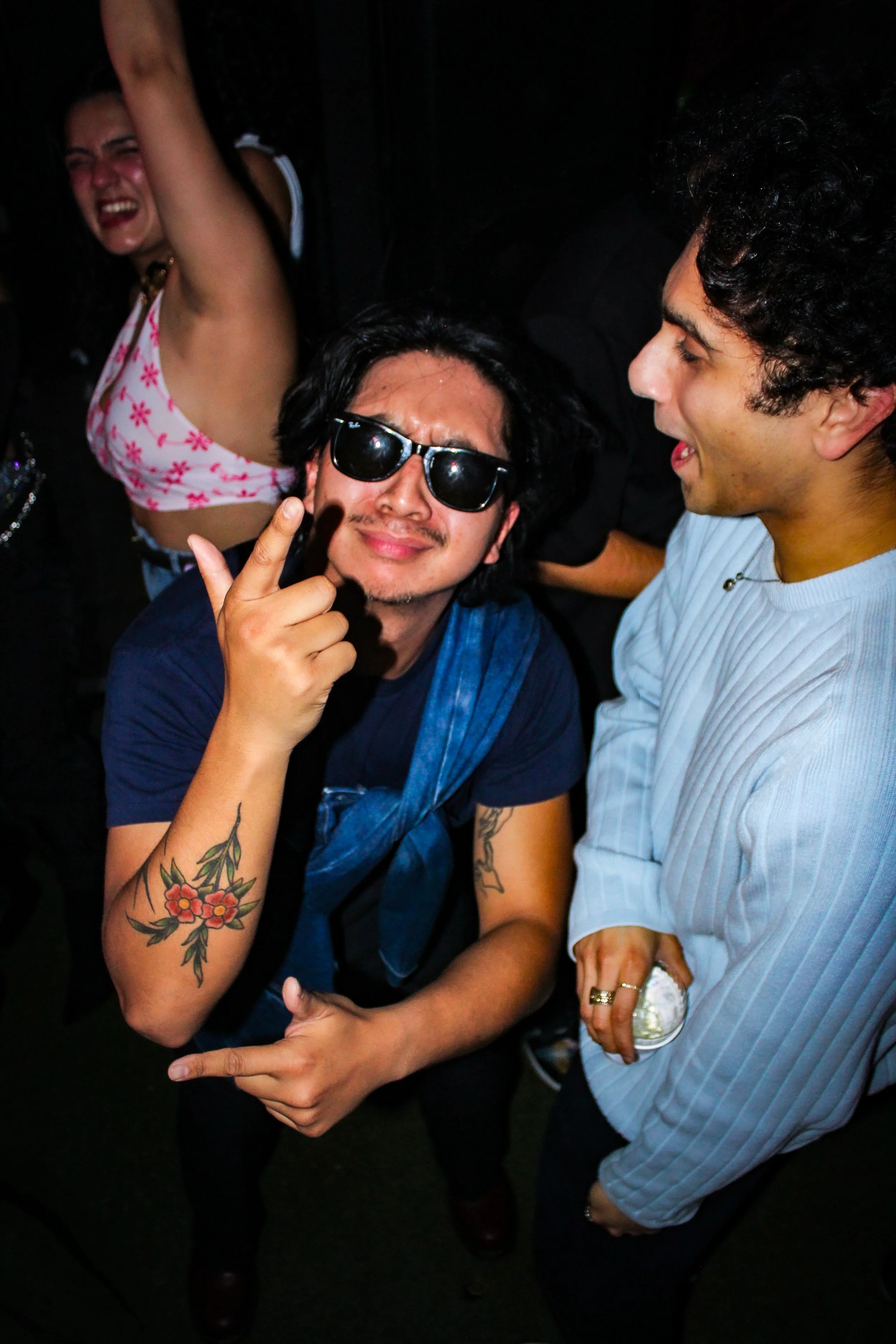Group of people at a party dancing and having fun, with one man making a peace sign and wearing sunglasses.