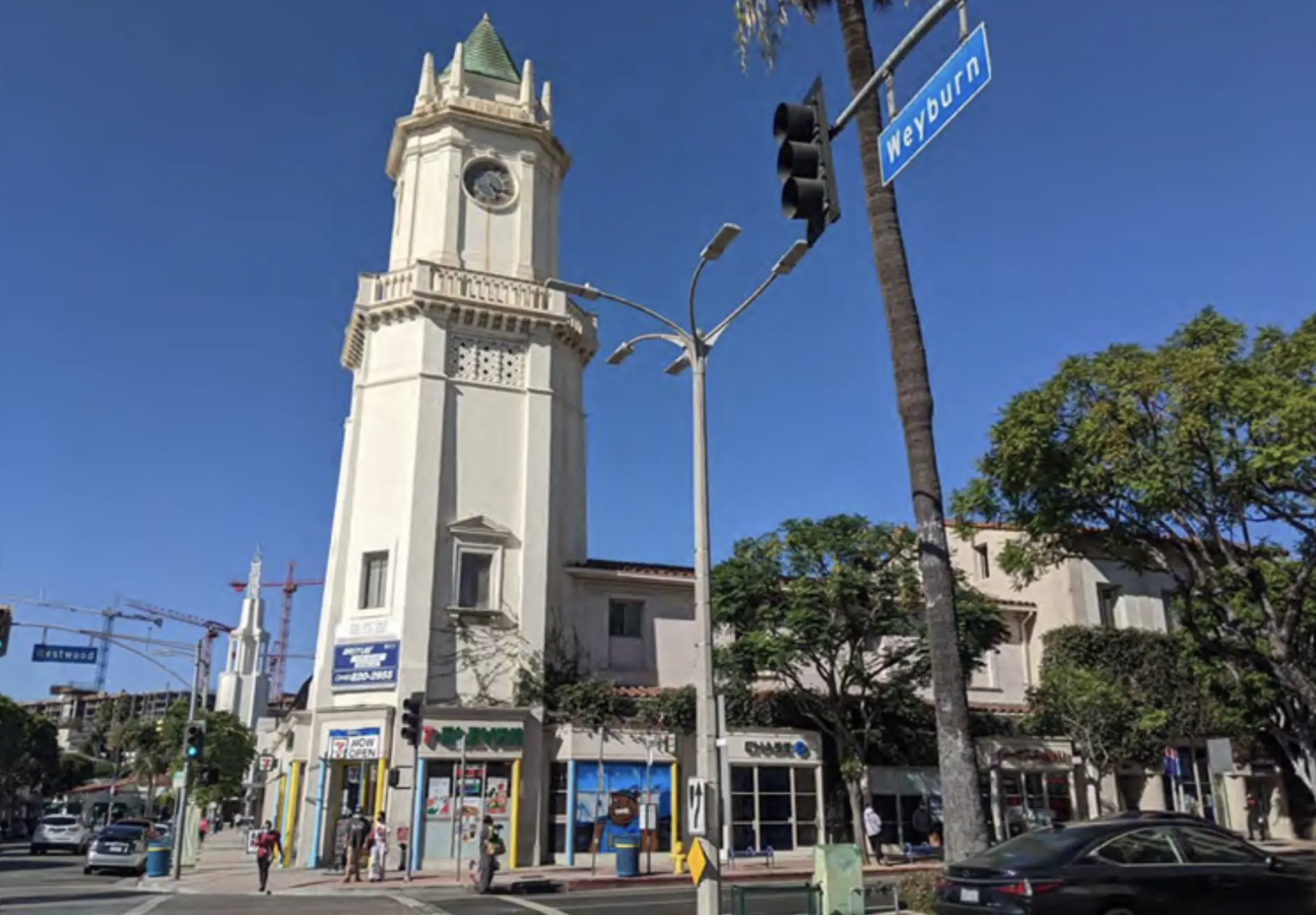 Street scene in San Francisco showing the historic Clock Tower on Market Street, with pedestrians, cars, and storefronts, including a 7-Eleven.