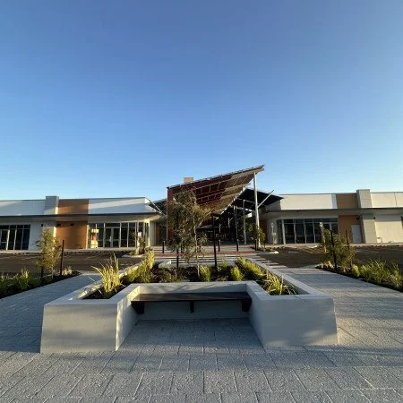 Modern building with solar panels on the roof, landscaped courtyard with seating and greenery under a clear blue sky.