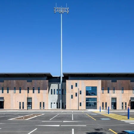 Empty parking lot in front of a large building with a tall light pole in the center and a clear blue sky.