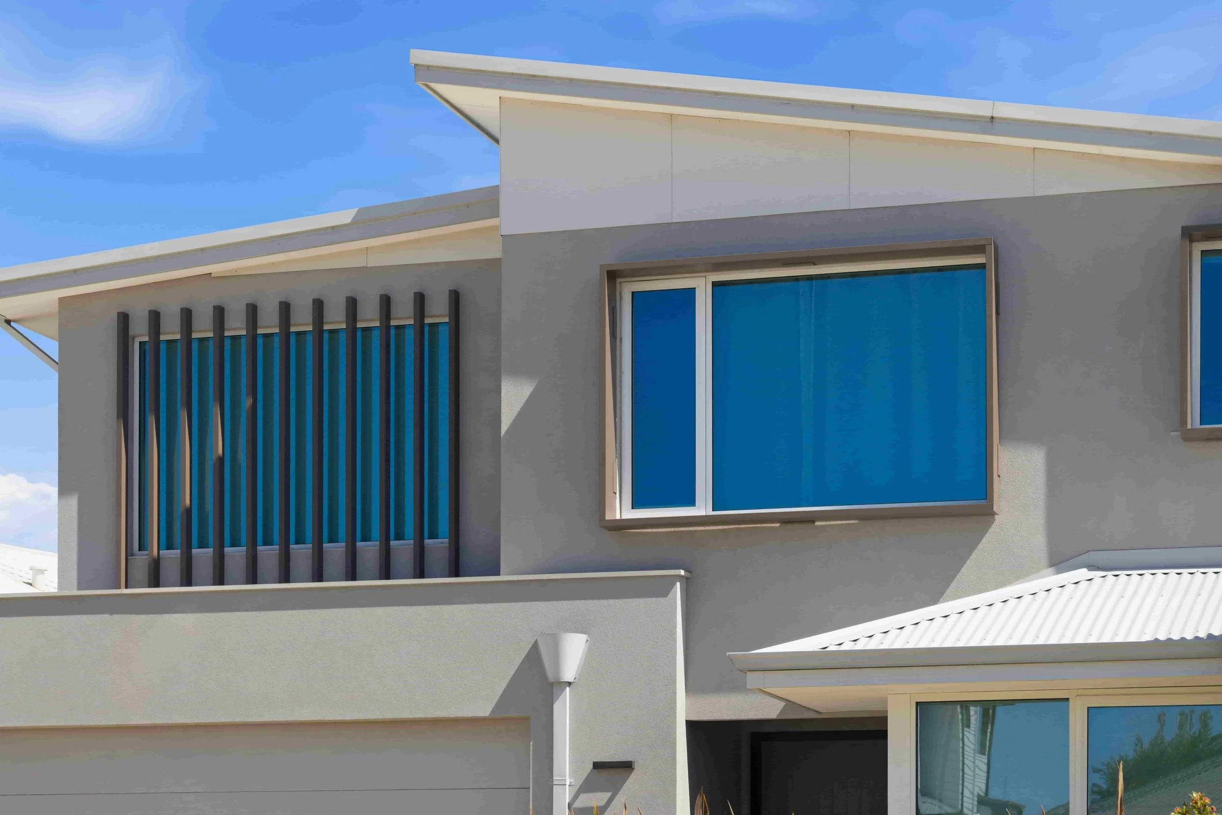 Modern house with large blue windows, angled roof, and a porch, under a clear blue sky.