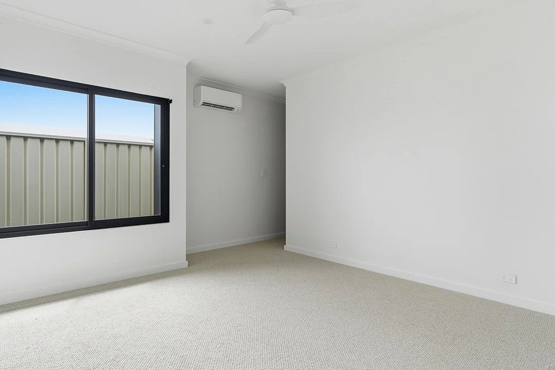 Empty room with a window, white walls, beige carpet, and air conditioning unit.