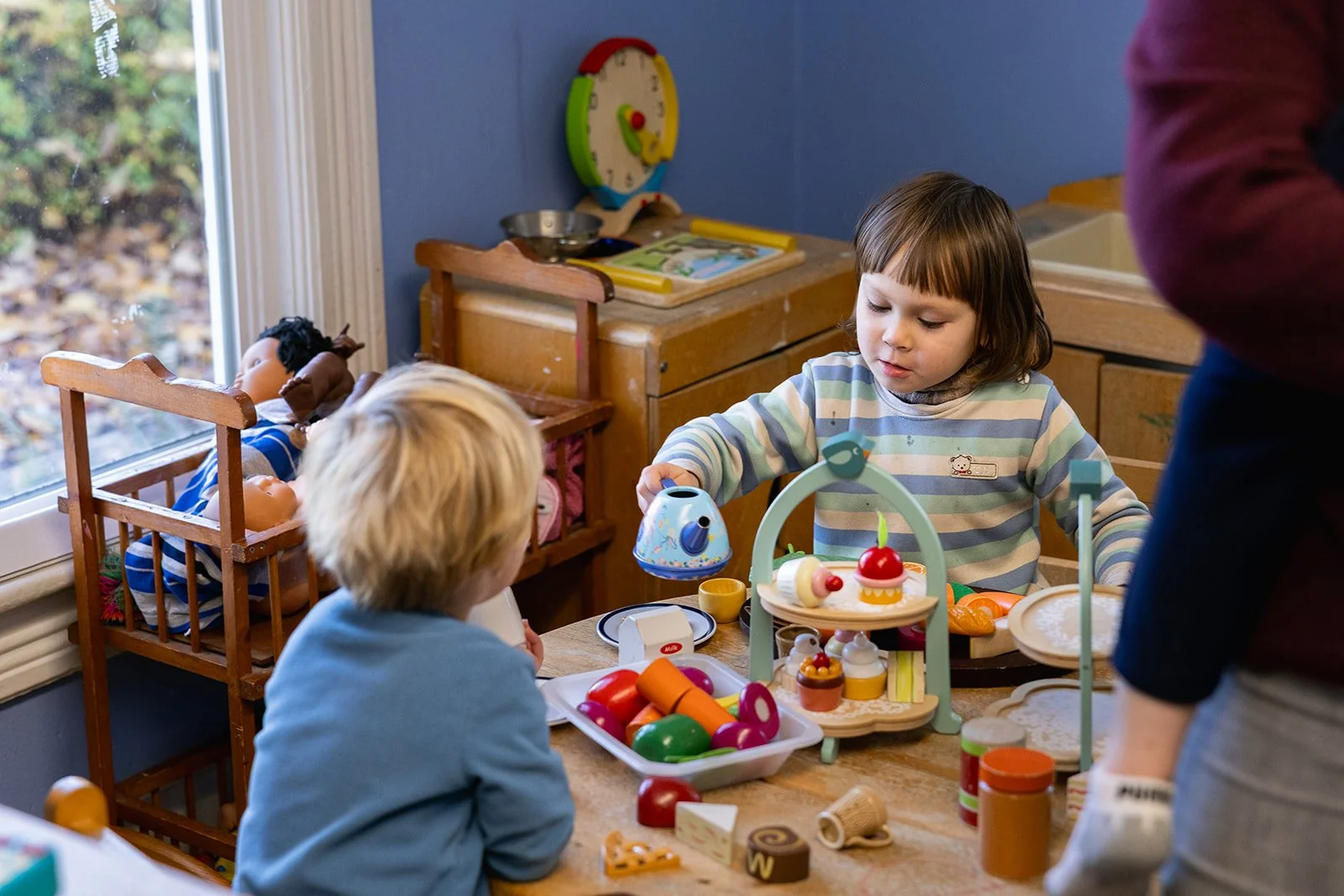 Two children playing at a table. One is acting like they are pouring tea for the other child.