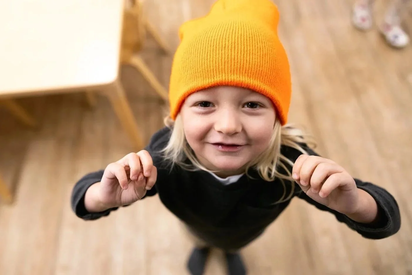 Preschooler smiling up at the camera. Blond hair, yellow knit cap, and blue sweater