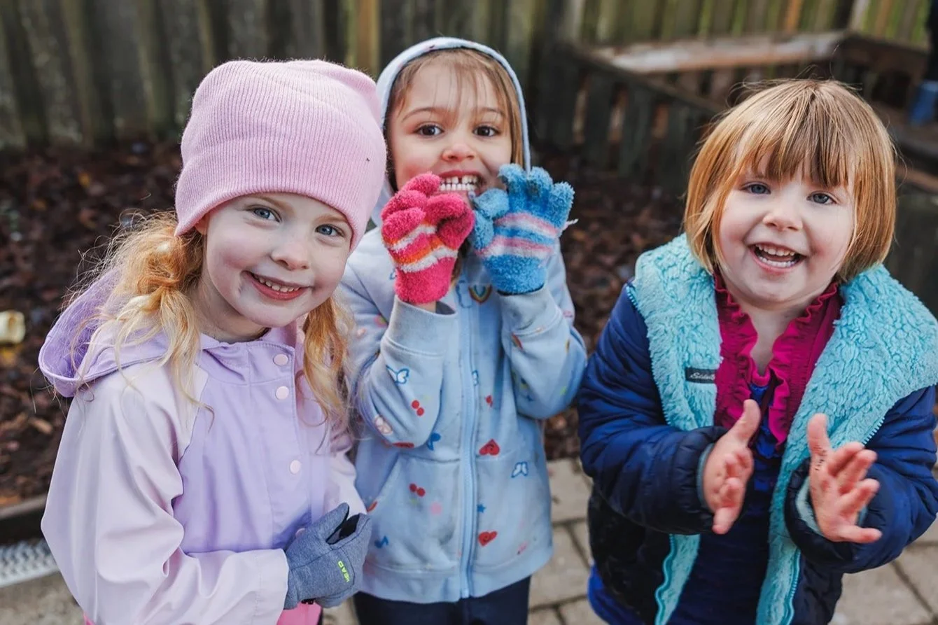 Three preschoolers smiling at camera with jackets and hats on