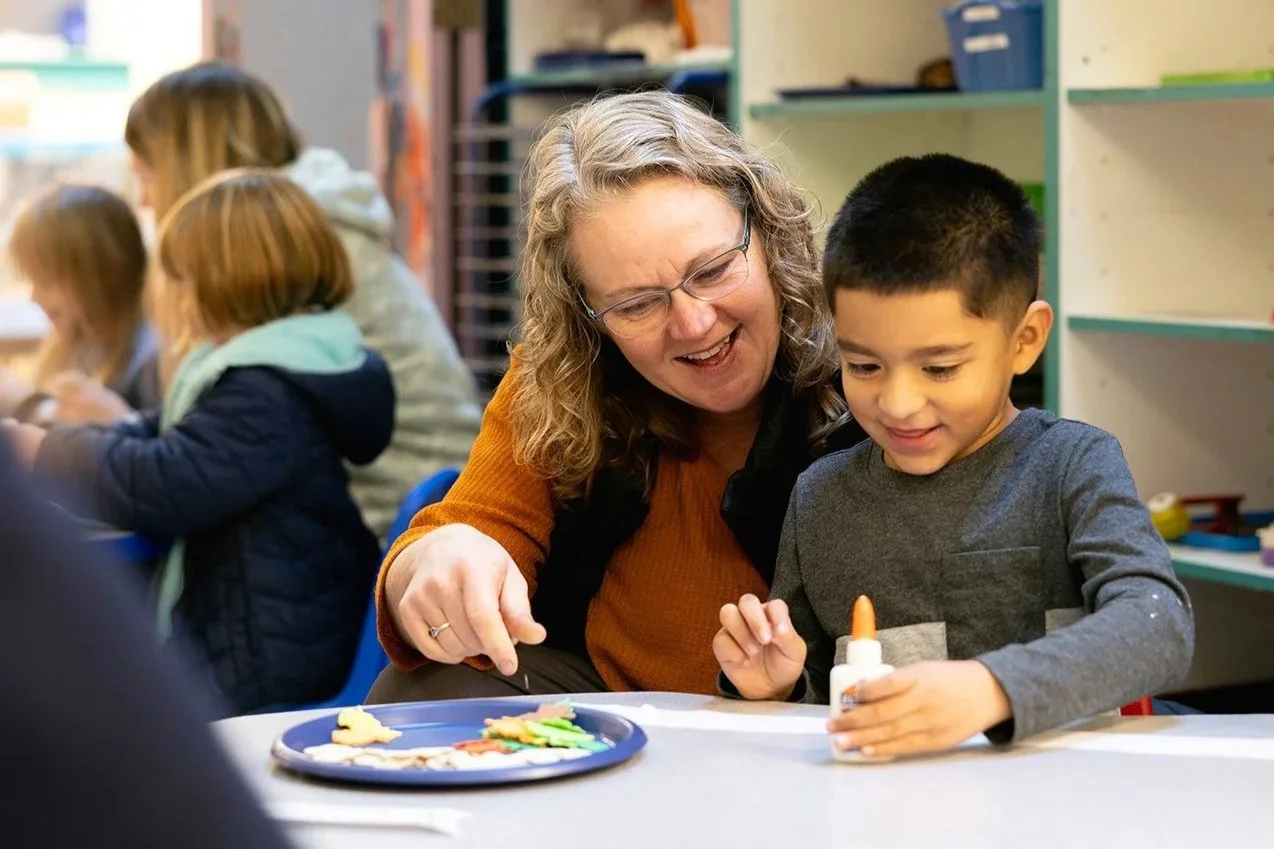 Preschooler sitting on teacher's lap. Both smiling. 