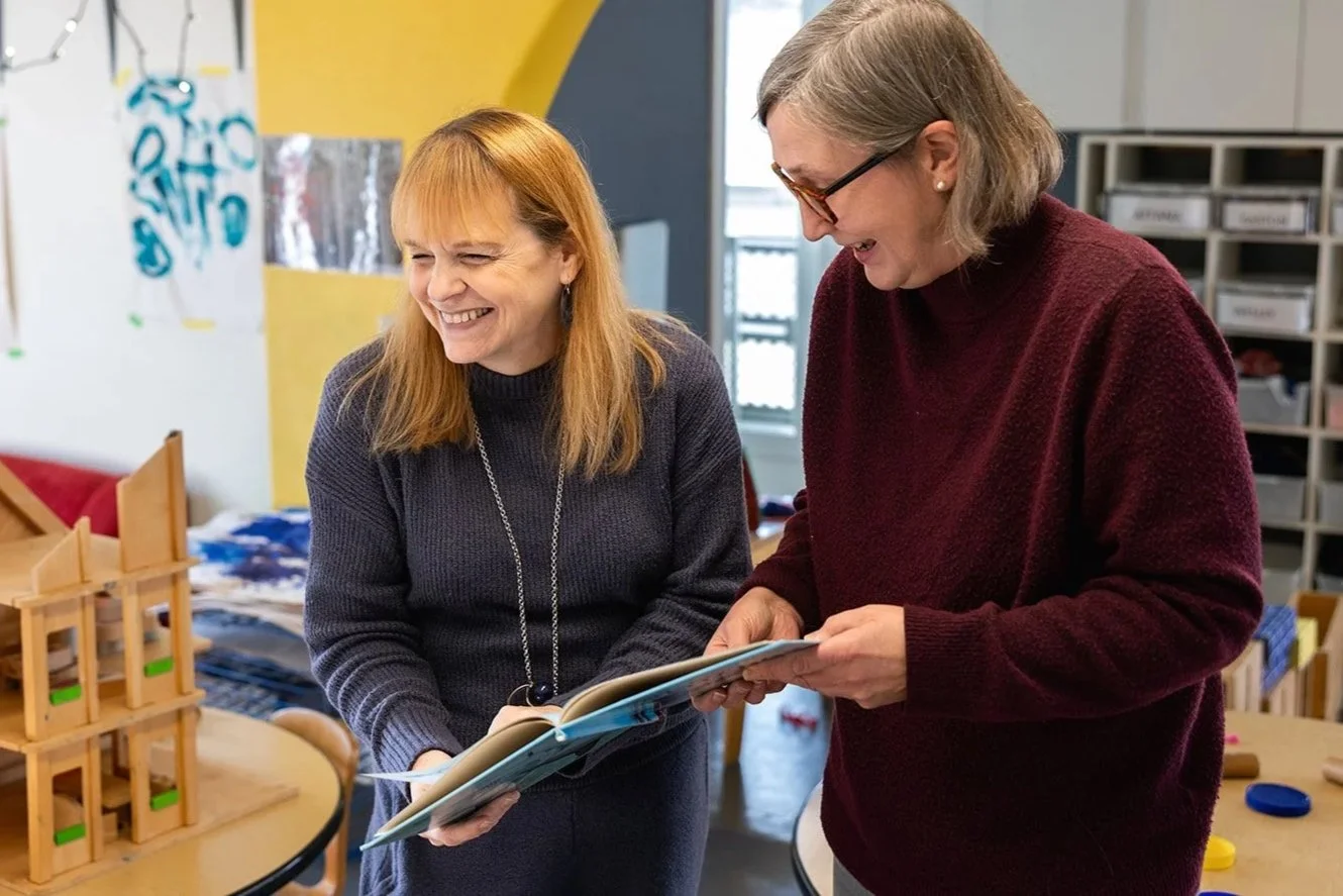 Two teachers laughing while holding a book