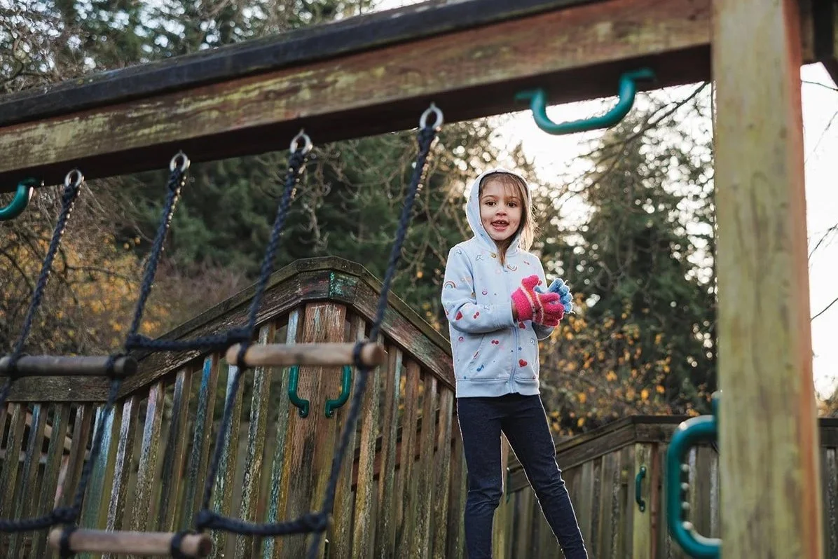 Chilld standing on a playground set black pants, blue hoodie, and red gloves
