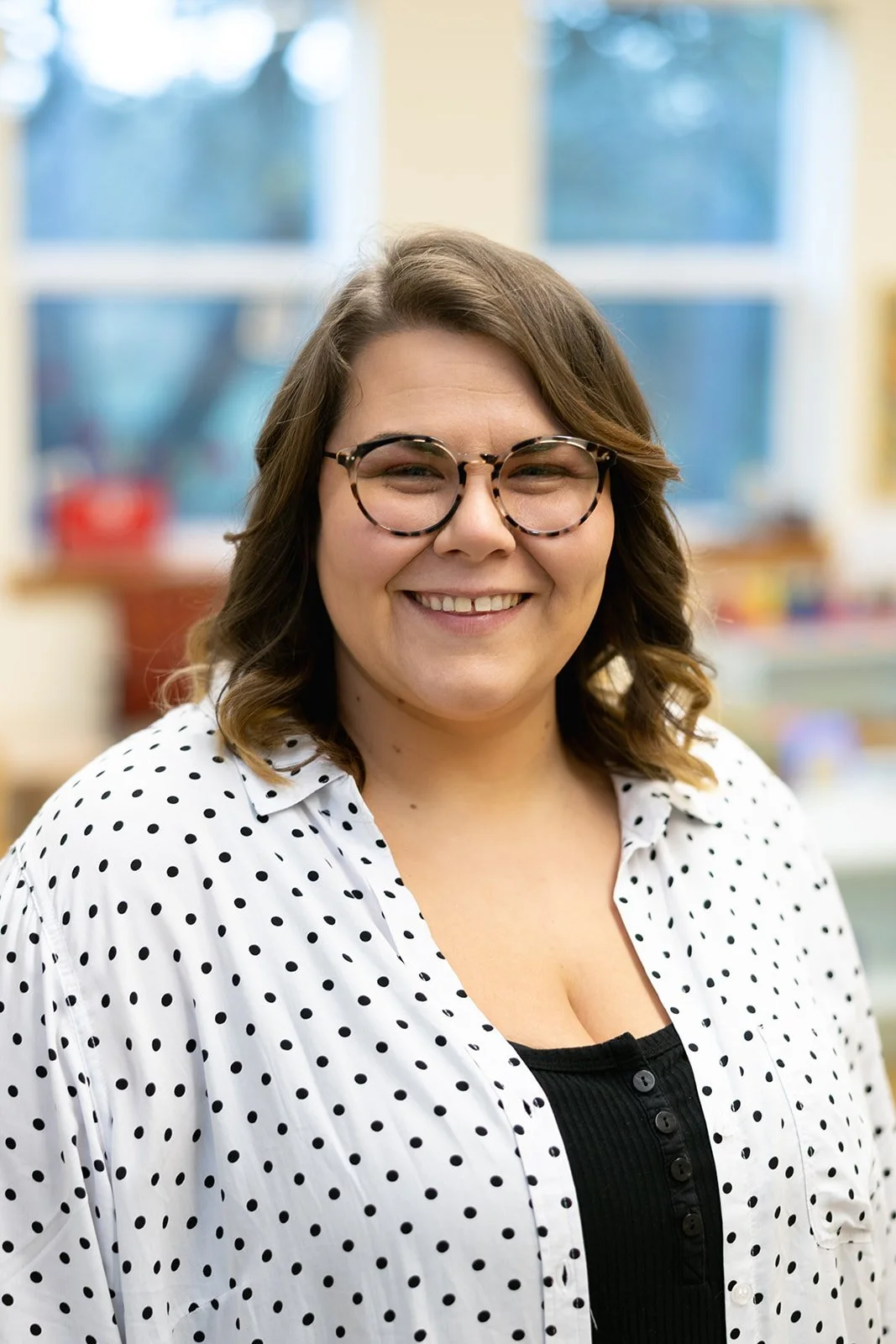 Portrait of person with brown hair and glasses wearing a while shirt with blue polka dots