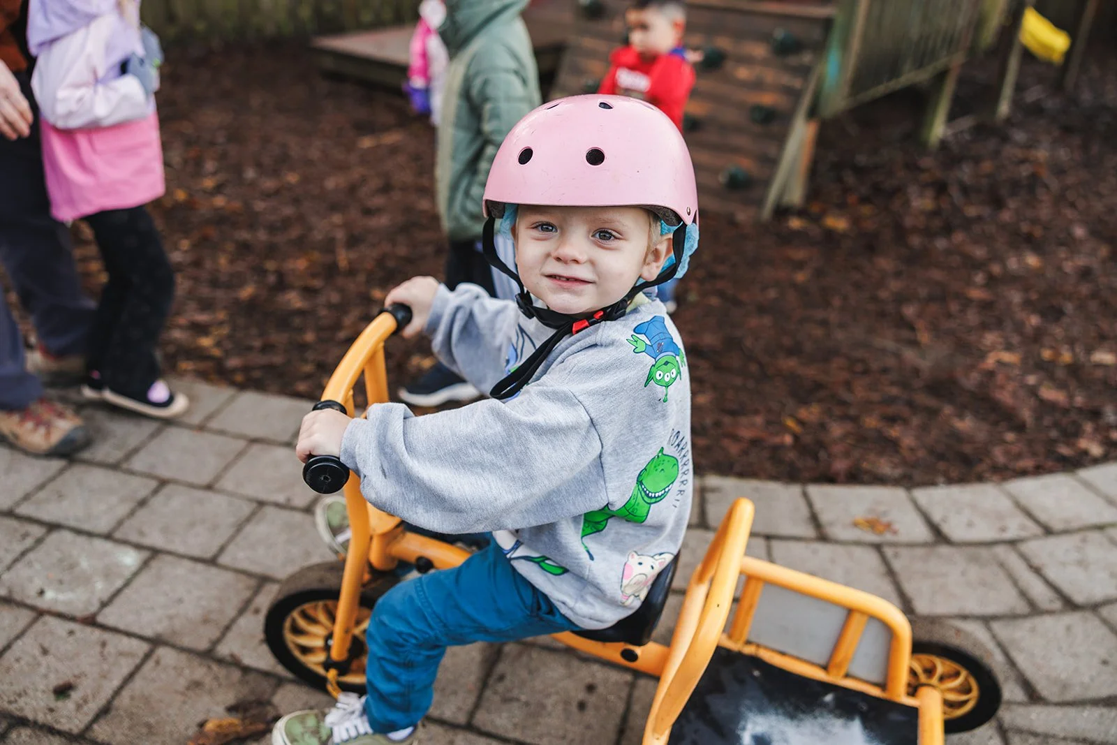 Kid wearing pink helmet looking at cameral sitting on a yellow bike