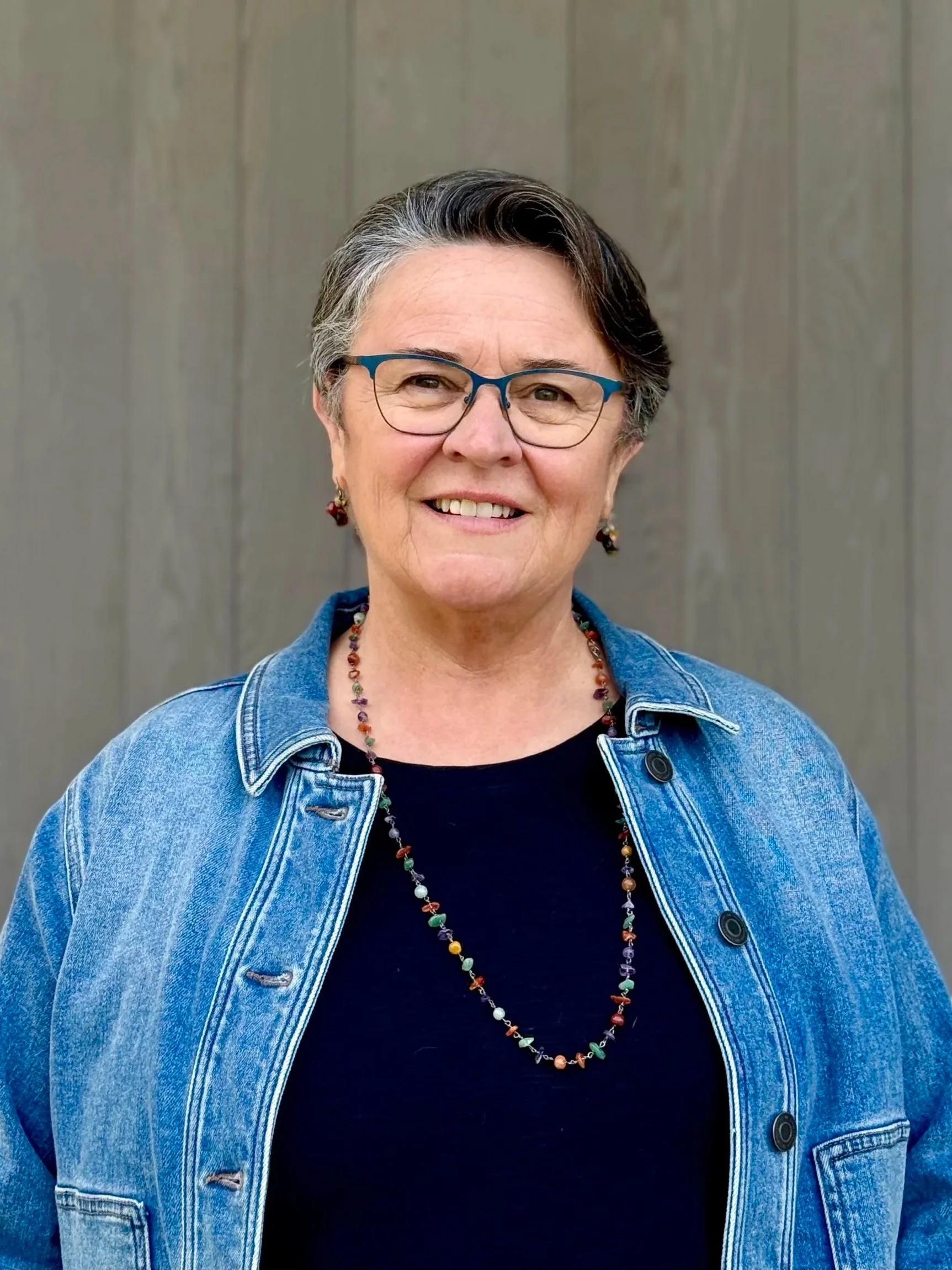 Portrait of person with short salt and pepper hair, dark shirt and jean jacket