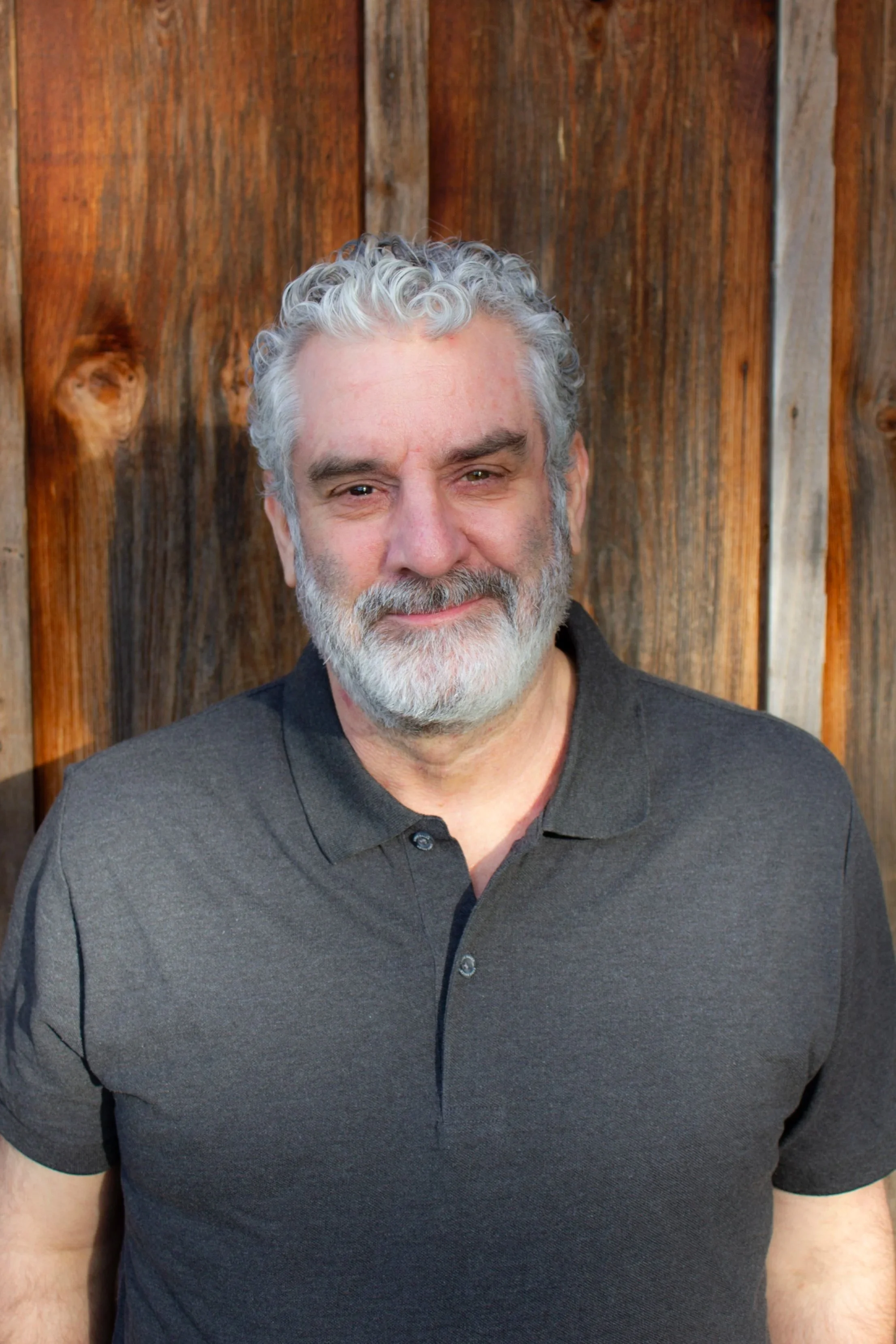 Portrait of person with short curly salt and pepper hair, beard, and mustache wearing a short sleeved grey collared shirt