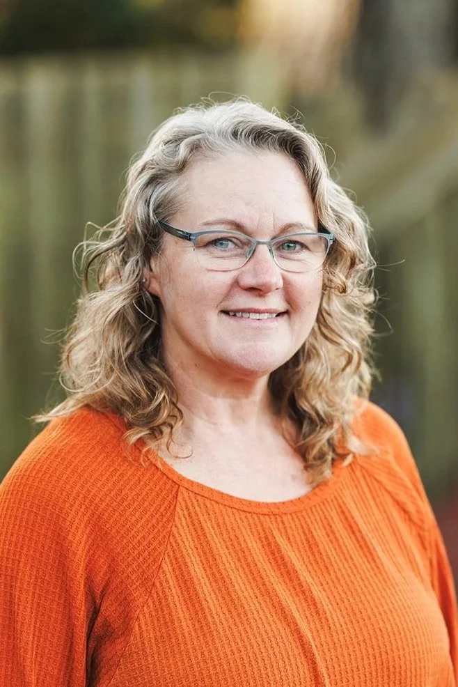 Portrait of person with long blond curly hair with glasses and orange blouse