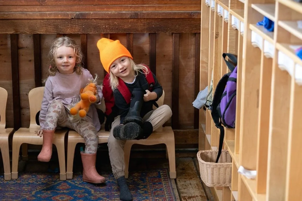Two kids looking at camera sitting down taking shoes off