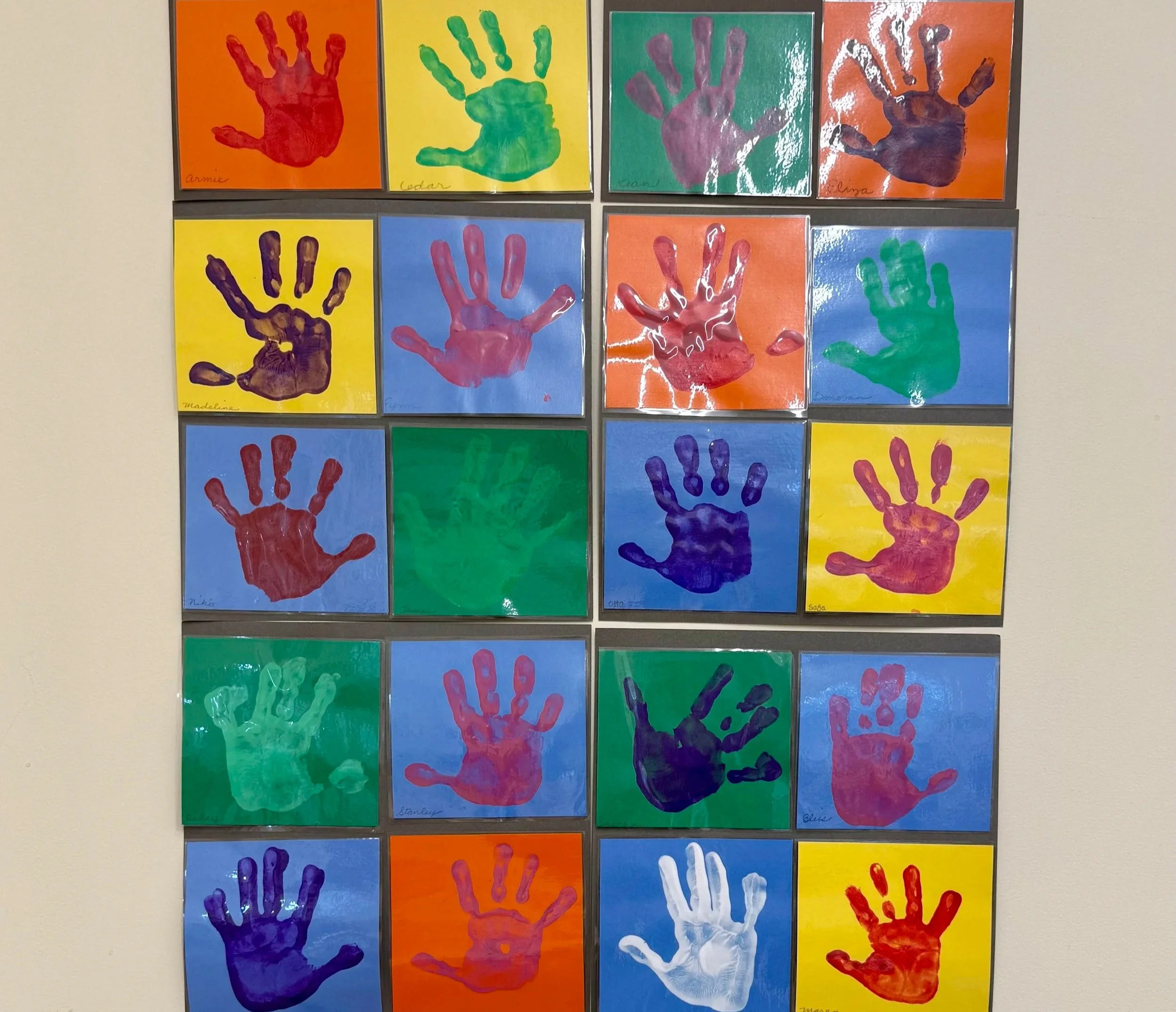 Grid of different colored painted hand prints on different colored paper