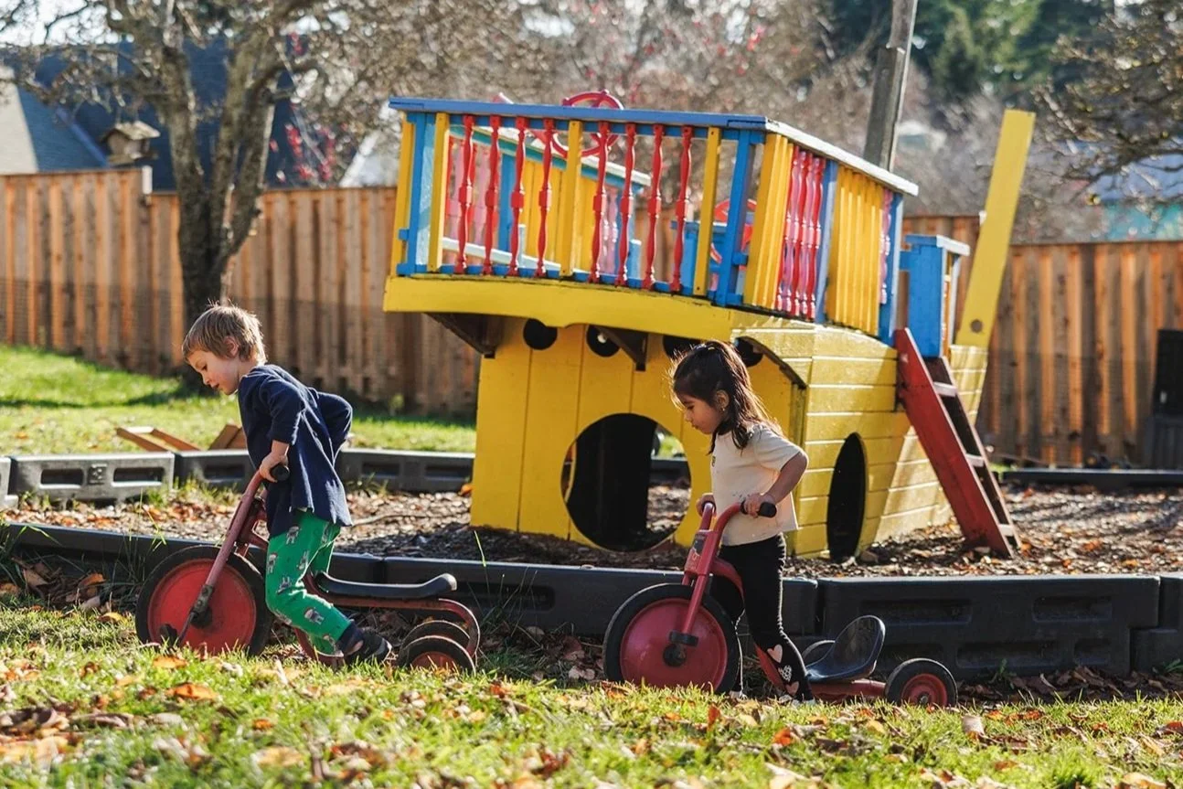 Two kids riding tricycles outside in a playground