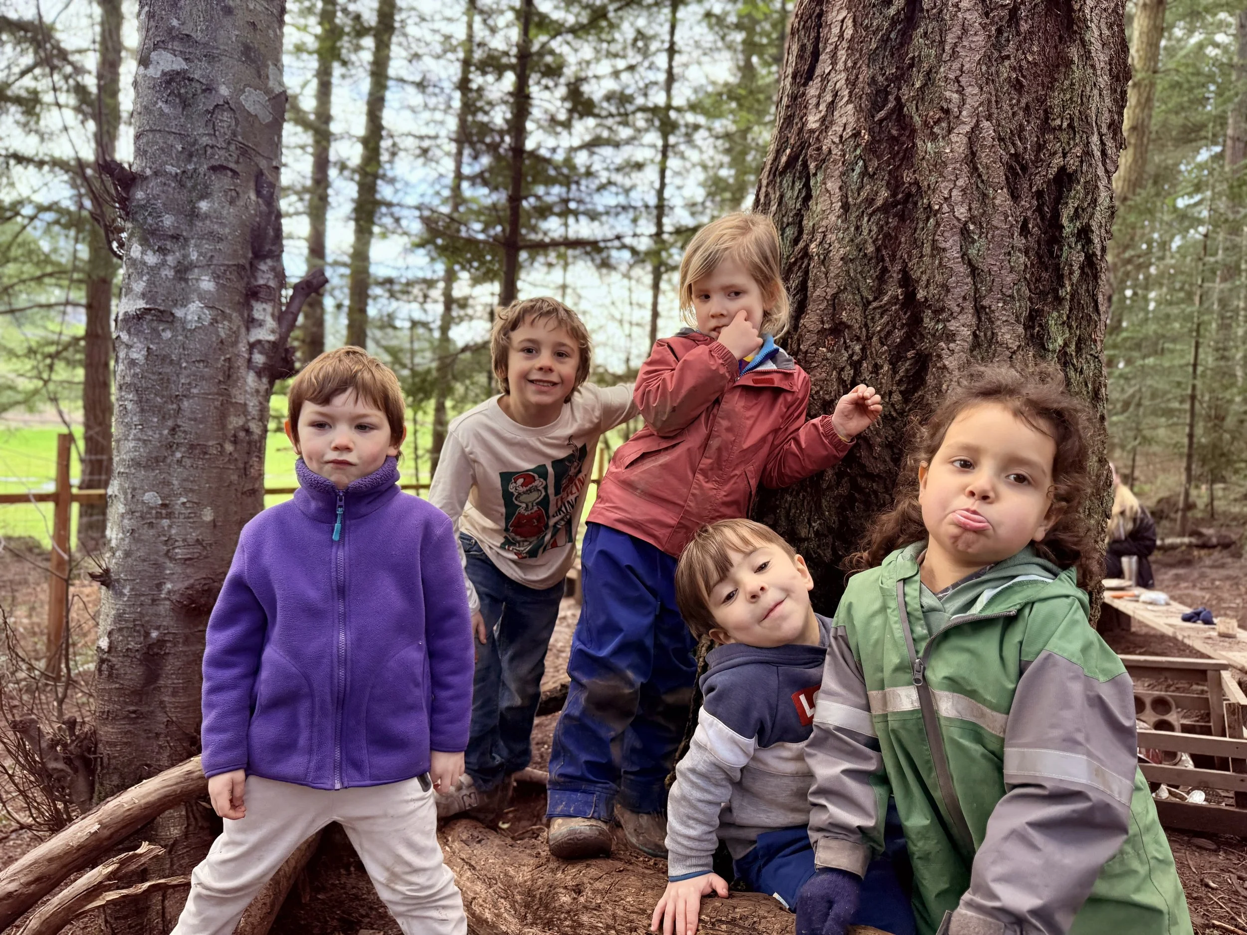 Five kids in the woods smiling and making funny faces at the camera
