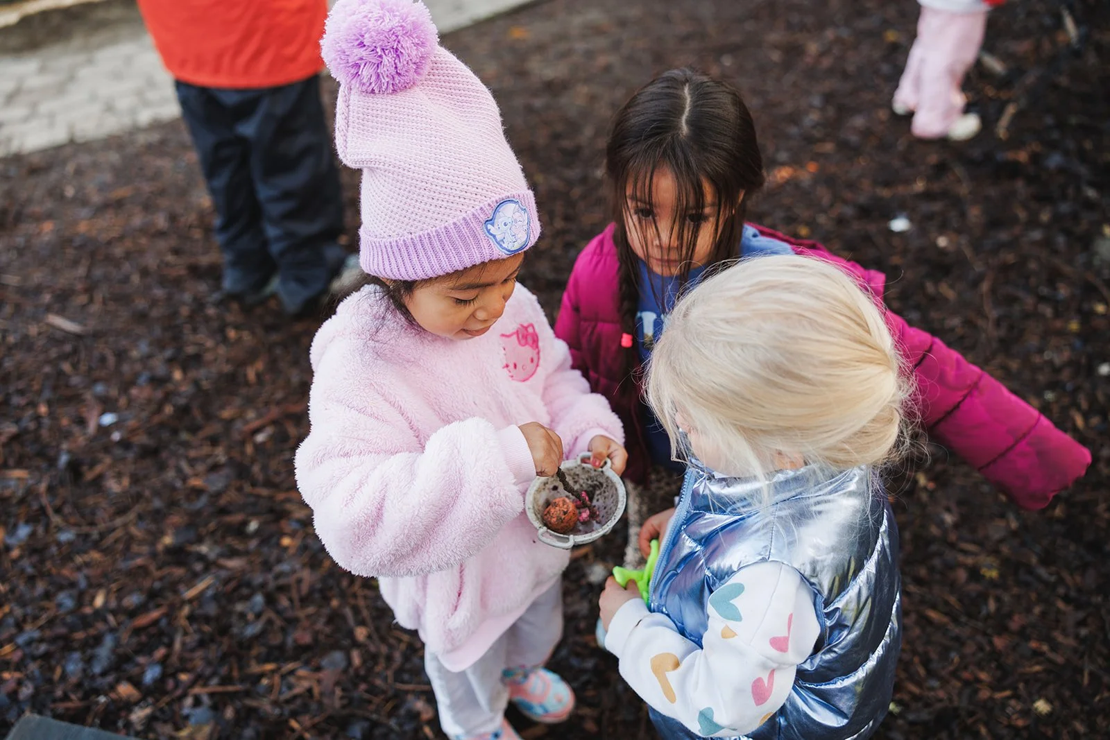 Three children outside from above holding a bowl in jackets and a hat