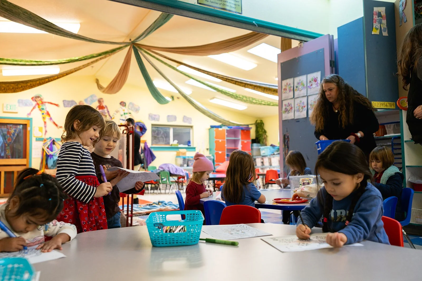 Classroom with multiple children in it with three drawing and two looking at a drawing together