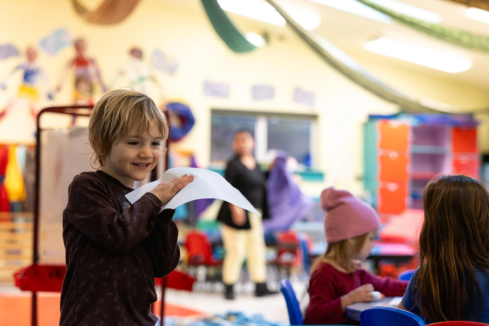 Preschooler smiling with blond hair holding a piece of paper between his hands