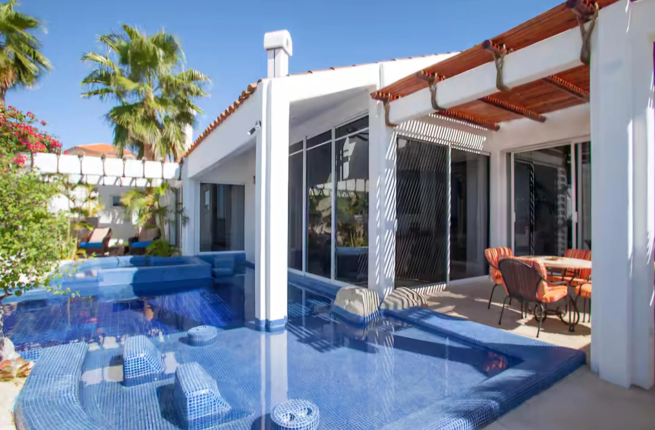 View of a house with a swimming pool in the backyard, outdoor patio furniture, and palm trees under a clear blue sky.