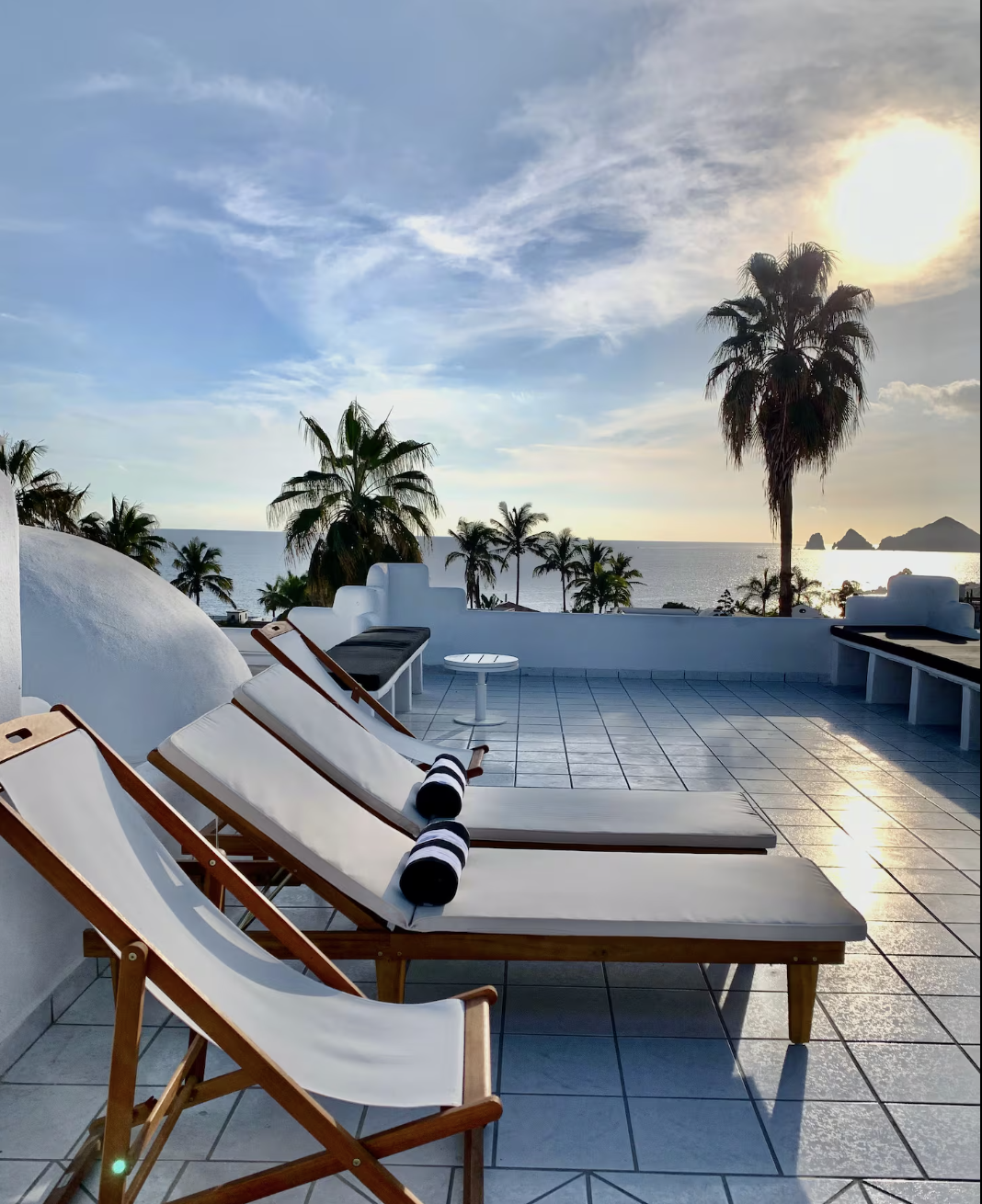People on a beach promenad with palm trees, walking,  sitting at benches, and enjoying the Cabo air with the ocean in the background. Seaside living in Cabo | The Marlin Hunter Fishing Charters and Luxury Villas
