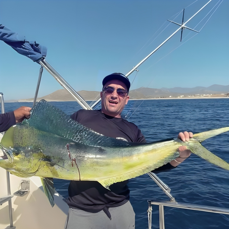 Man holding a large yellow and blue fish on a boat with water and mountains in the background. The Marlin Hunter fishing charter adventure
