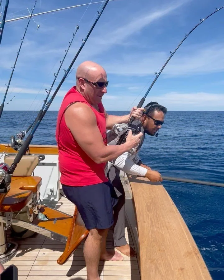 Two men fishing on a boat in the Baja peninsula under a blue sky, daytime. | The Marlin Hunter Fishing Charter Day Trip from Cabo