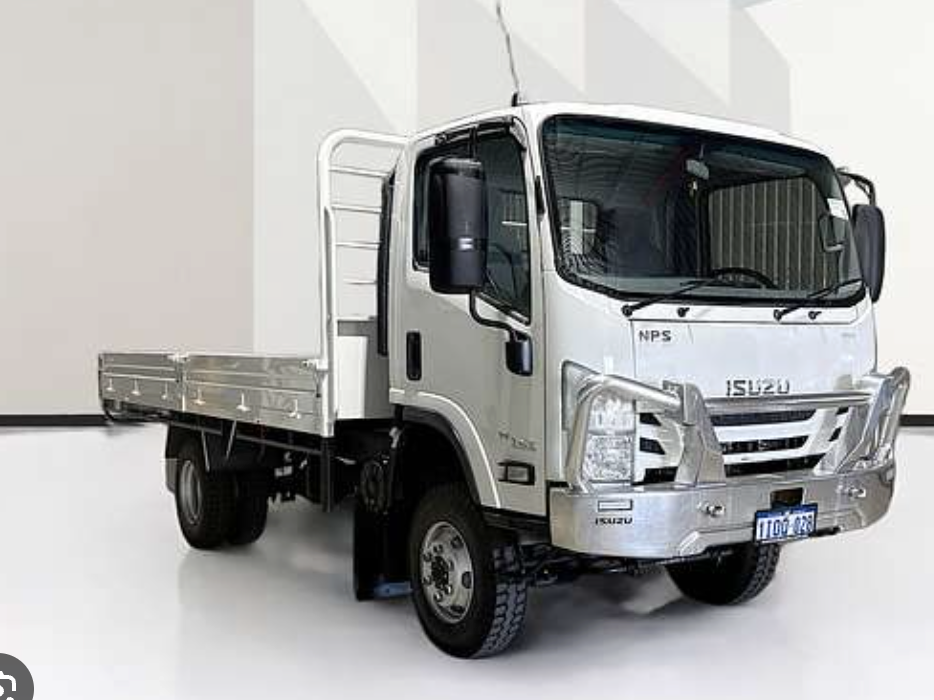 A white Isuzu flatbed truck parked indoors on a reflective floor, against a white wall with geometric shadows.