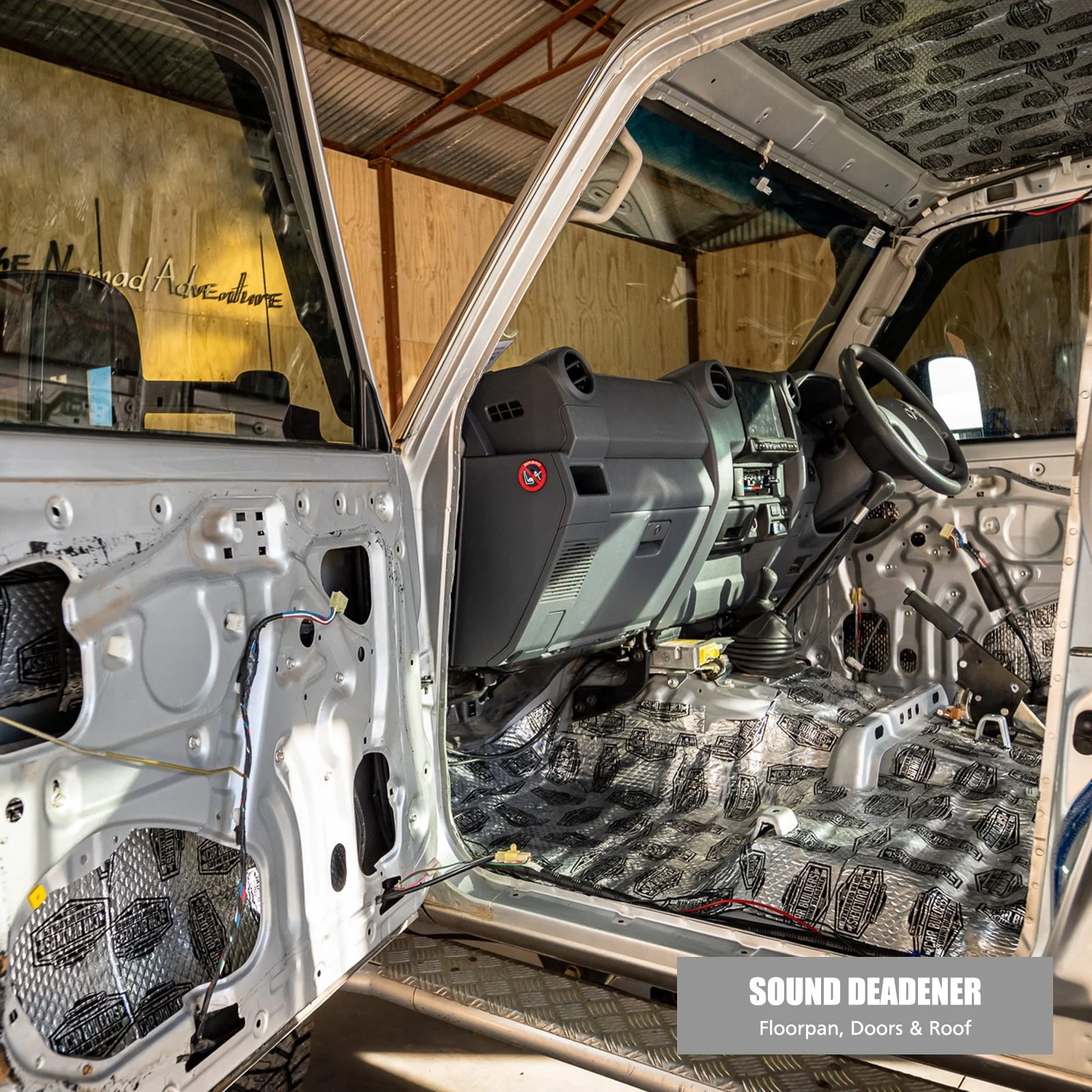 The interior of a vehicle undergoing sound deadening installation, with no doors or roof, showing soundproofing material on the floor and panels.