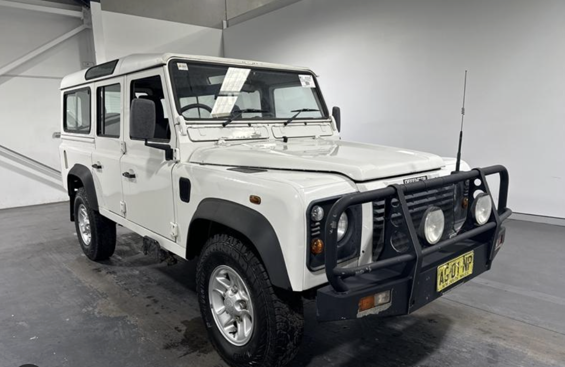 White Land Rover Defender with black front bumper guard and large off-road tires inside a garage.