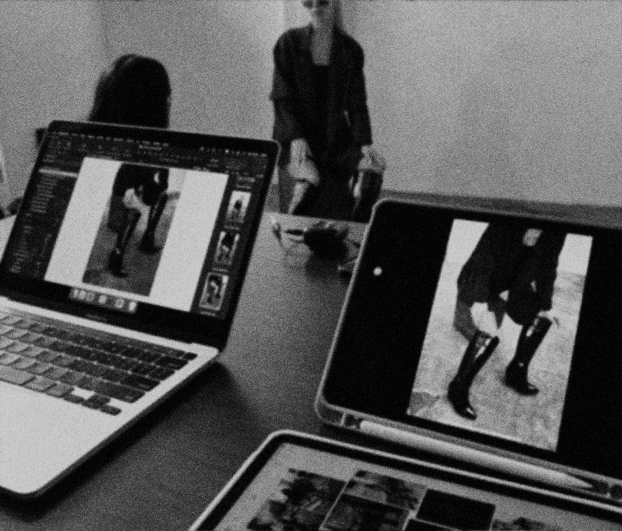 Photograph of a workspace with a laptop, a tablet, and smartphones displaying photos being taken in the moment of a model sitting on a bench. Indoor photoshoot for a shoe brand marketing campaign.