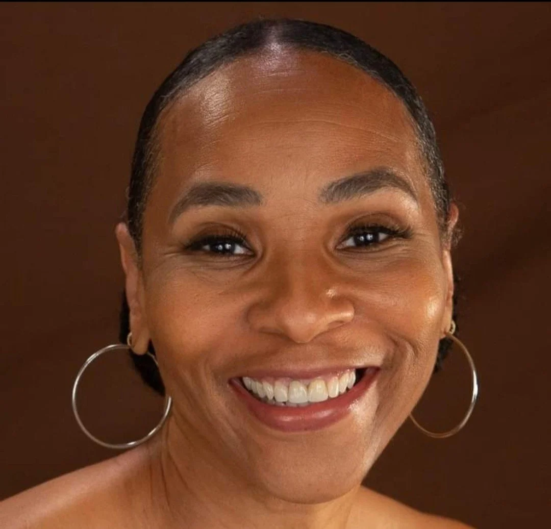 A close-up of a smiling woman with hoop earrings, natural makeup, and short dark hair.
