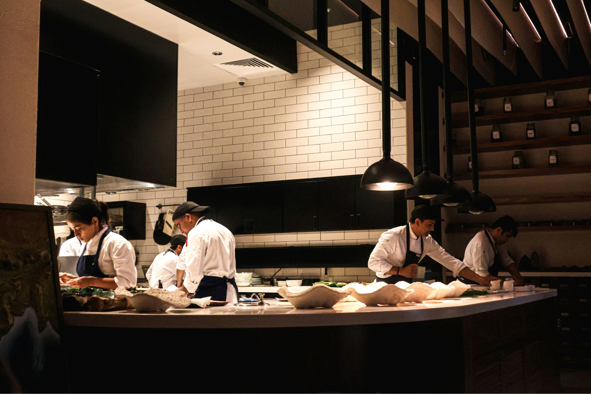 Chefs working in a modern restaurant kitchen with black and white decor, preparing dishes behind a curved counter.