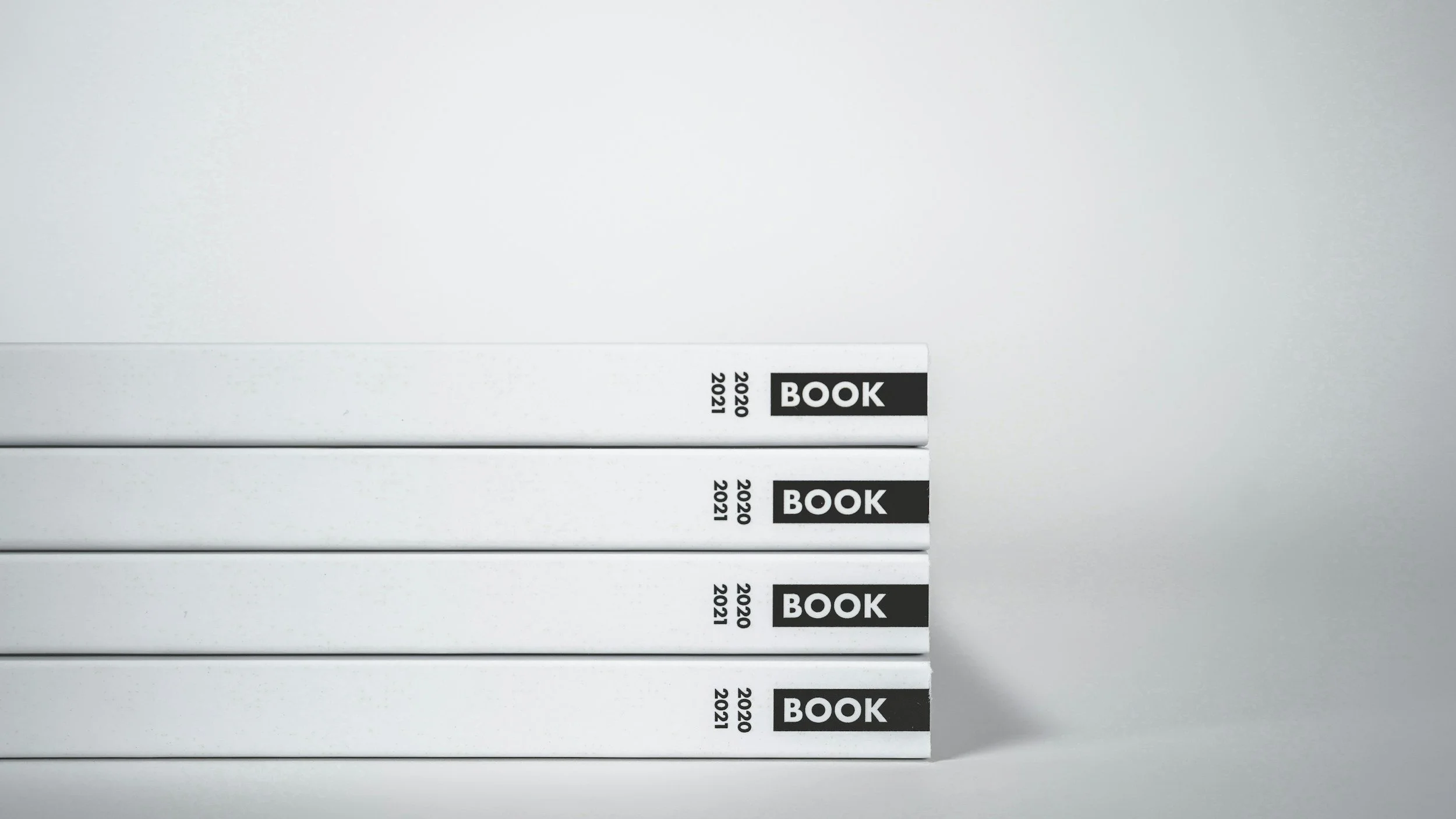 Stack of four white books with black labels reading 'BOOK', labeled with '2020-2021' on side, against a plain light gray background.