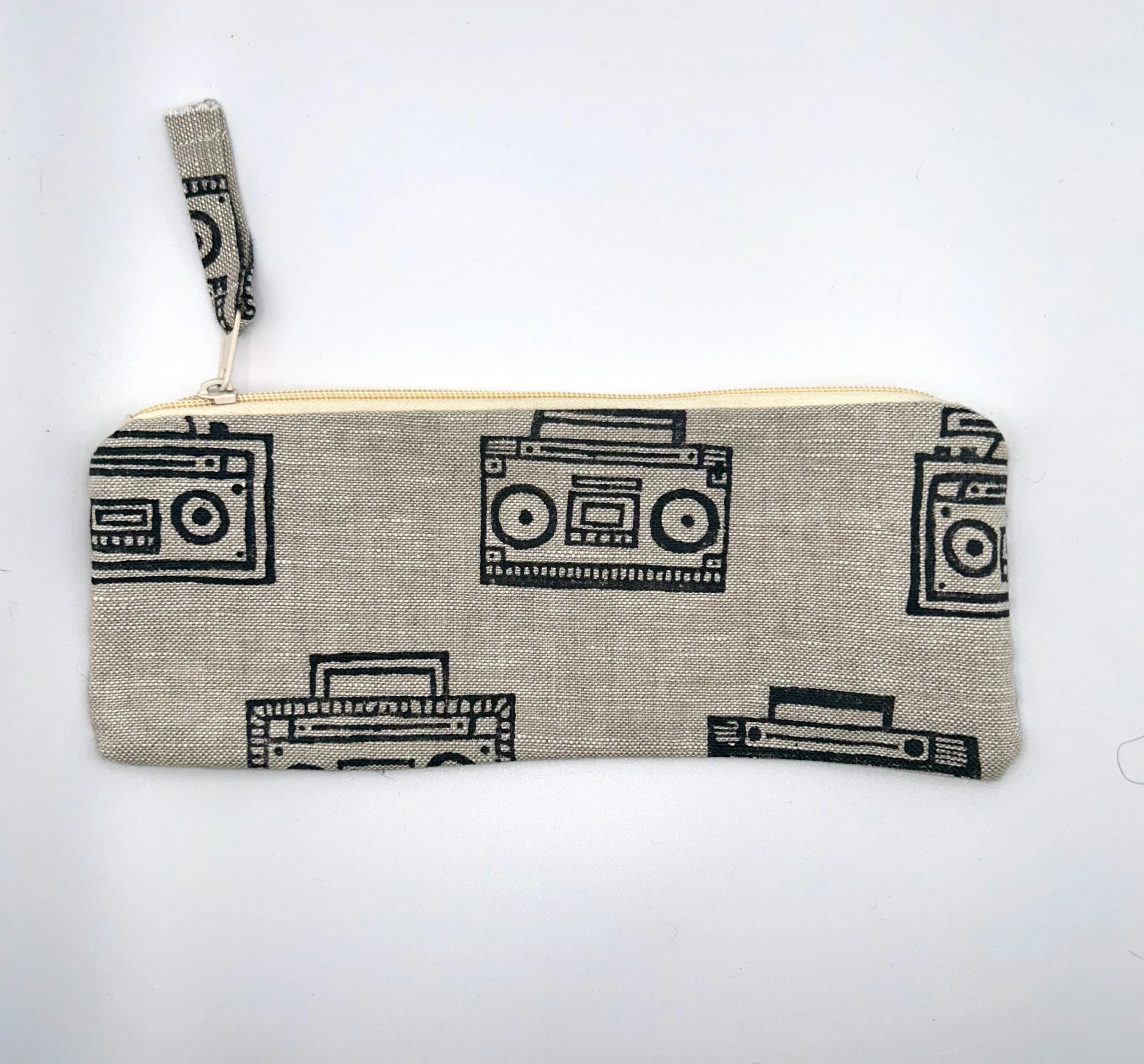 Close-up of a fabric bag with a black print of various stereo and audio equipment. The bag has a beige background and a white zipper along the top edge.