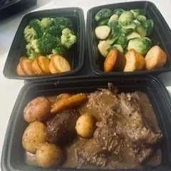 A three-compartment black meal container with vegetables in the top left section, chicken in the top right section, and roasted potatoes with beef stew in the bottom section.