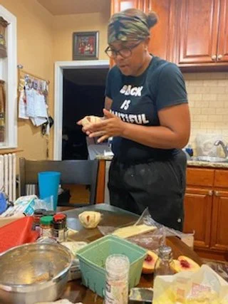 Chef Roxx, wearing glasses and a headband, preparing food in a kitchen.