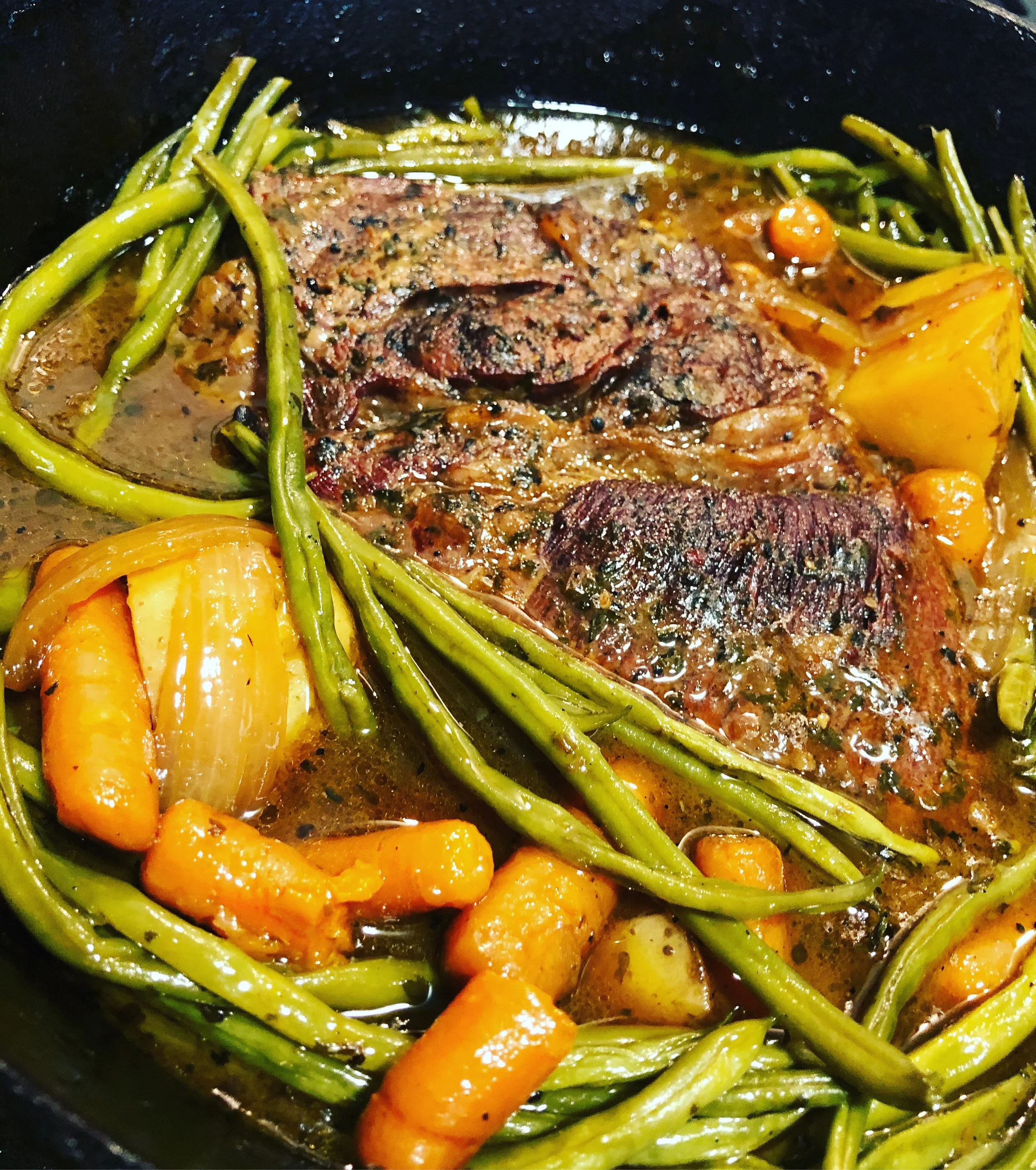 Cooked meat with vegetables including carrots, onions, and green beans in a skillet