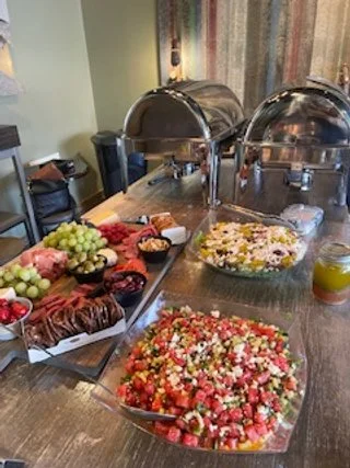 Buffet table with fresh fruit, assorted desserts, and two chafing dishes in a dining room.